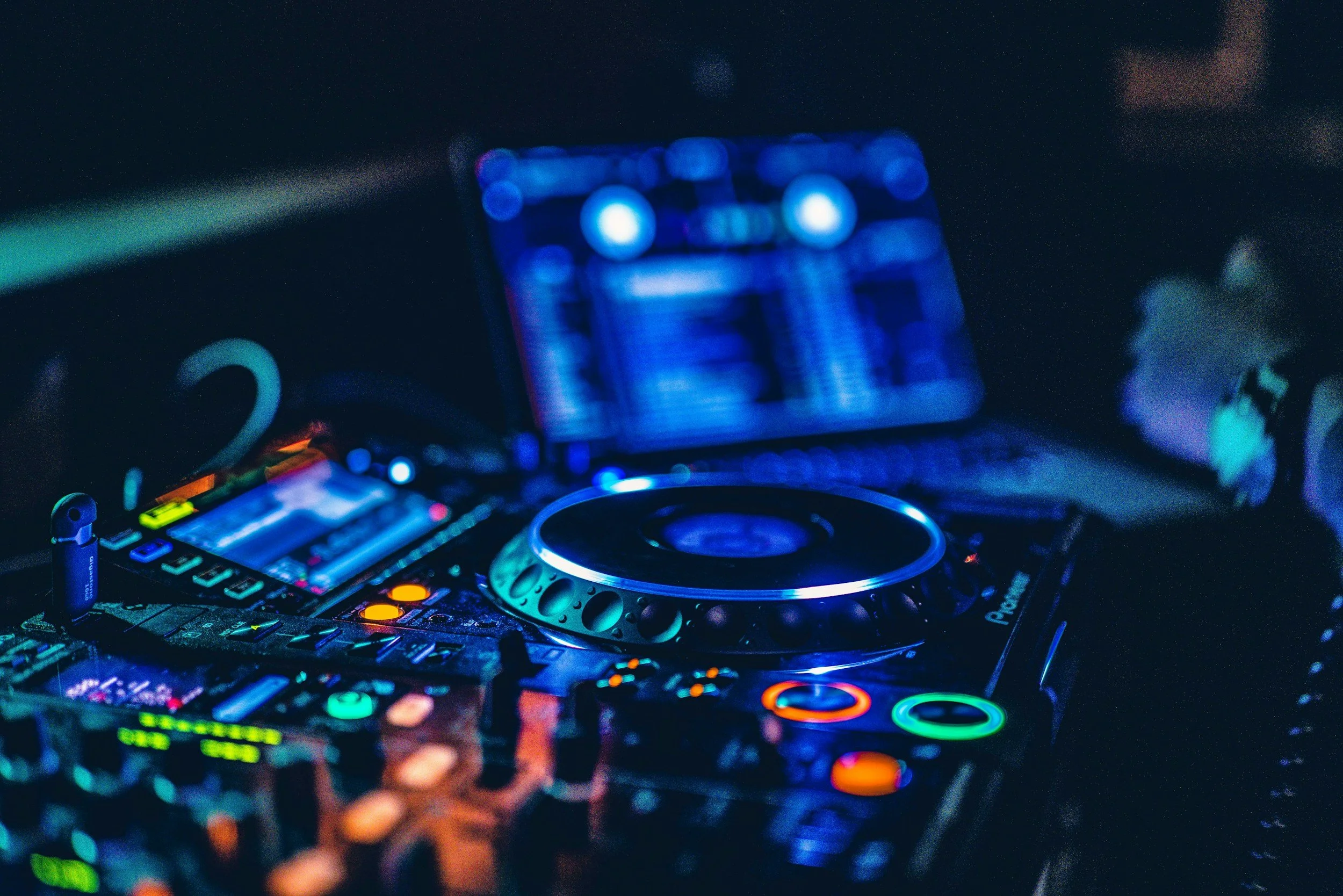 A DJ setup with turntables, a mixer, and a laptop in a dark environment with colorful LED lights.