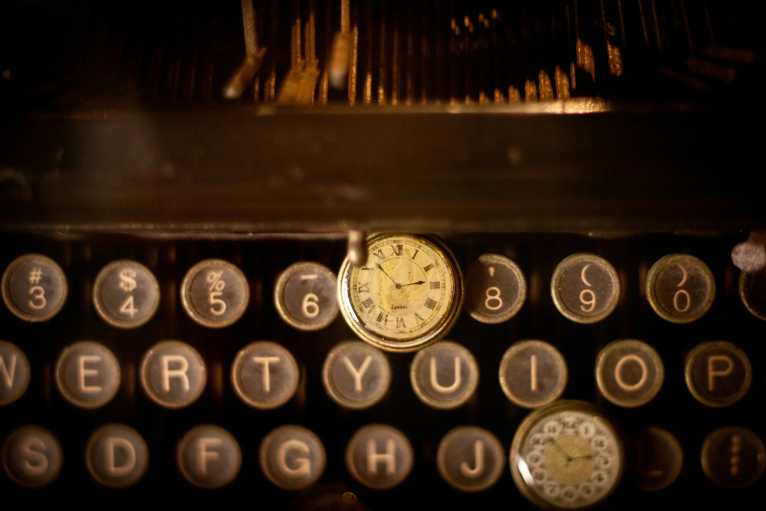 A photo in sepia tone of part of an old typewriter. There is also an antique fob watch on top of the keys. Image by Cliff Johnson on Unsplash.