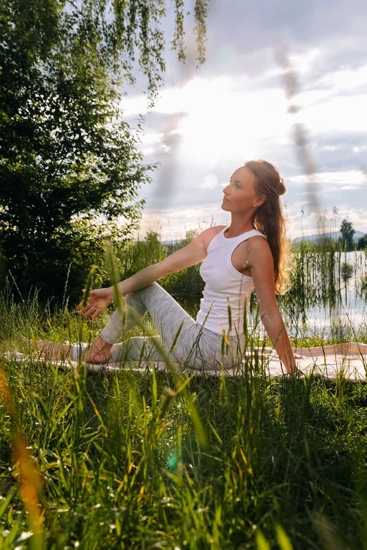 Frau macht Pilates am See bei Sonnenuntergang, umgeben von Natur.