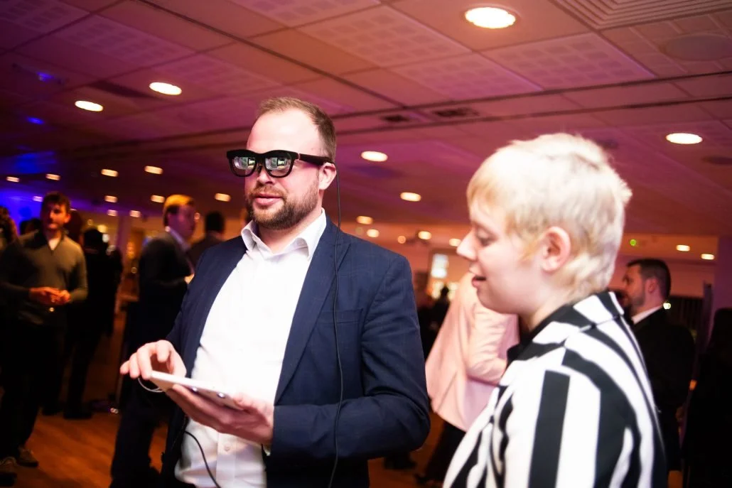 a photo of a man and a woman looking at a white mobile phone. the man is wearing a pair of smart glasses