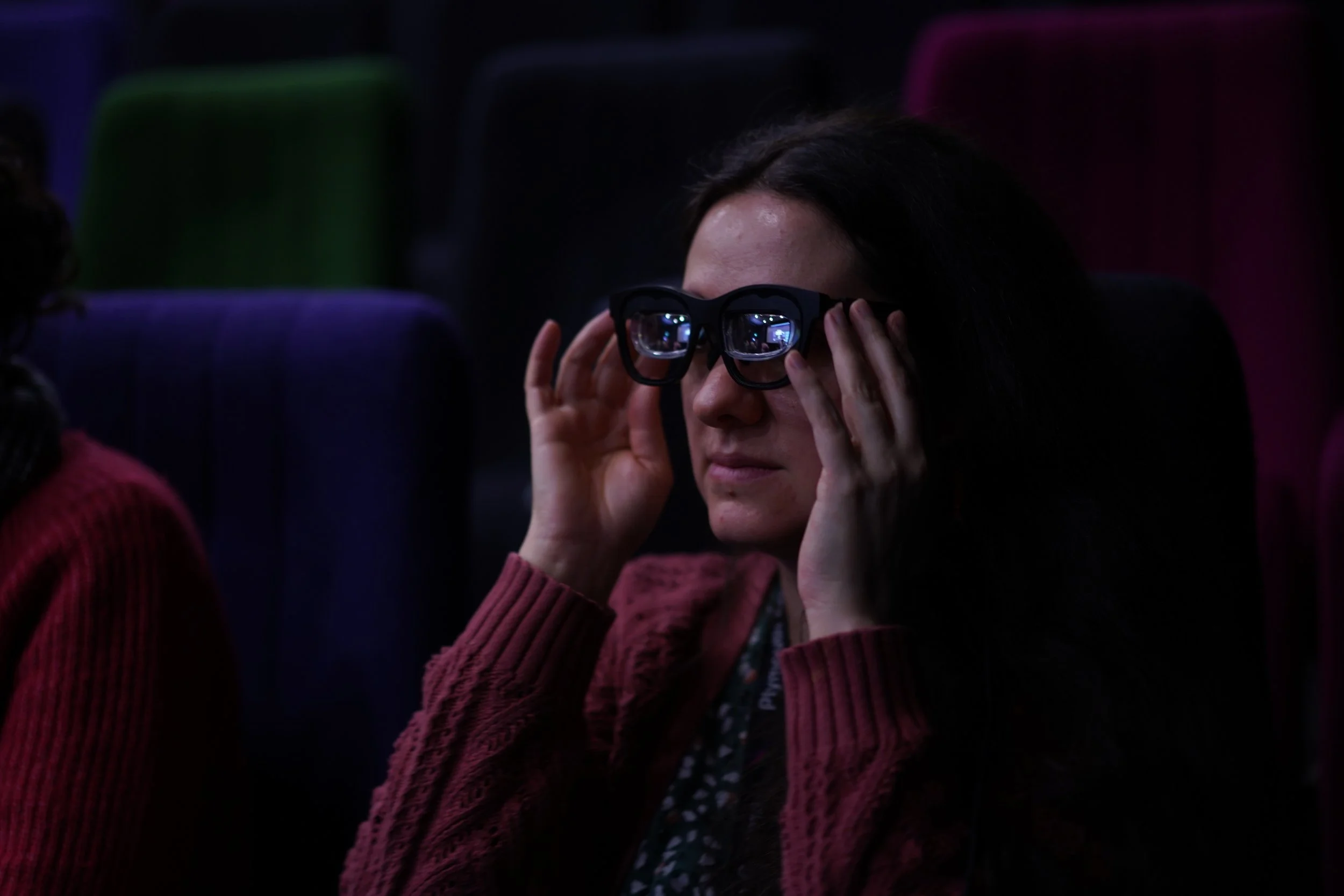 A close up of a woman with long dark hair holding the smart glasses up to her face