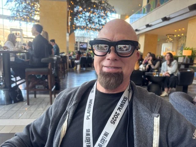 A man in a grey hoodie and white SXSW lanyard wearing a pair of smart glasses