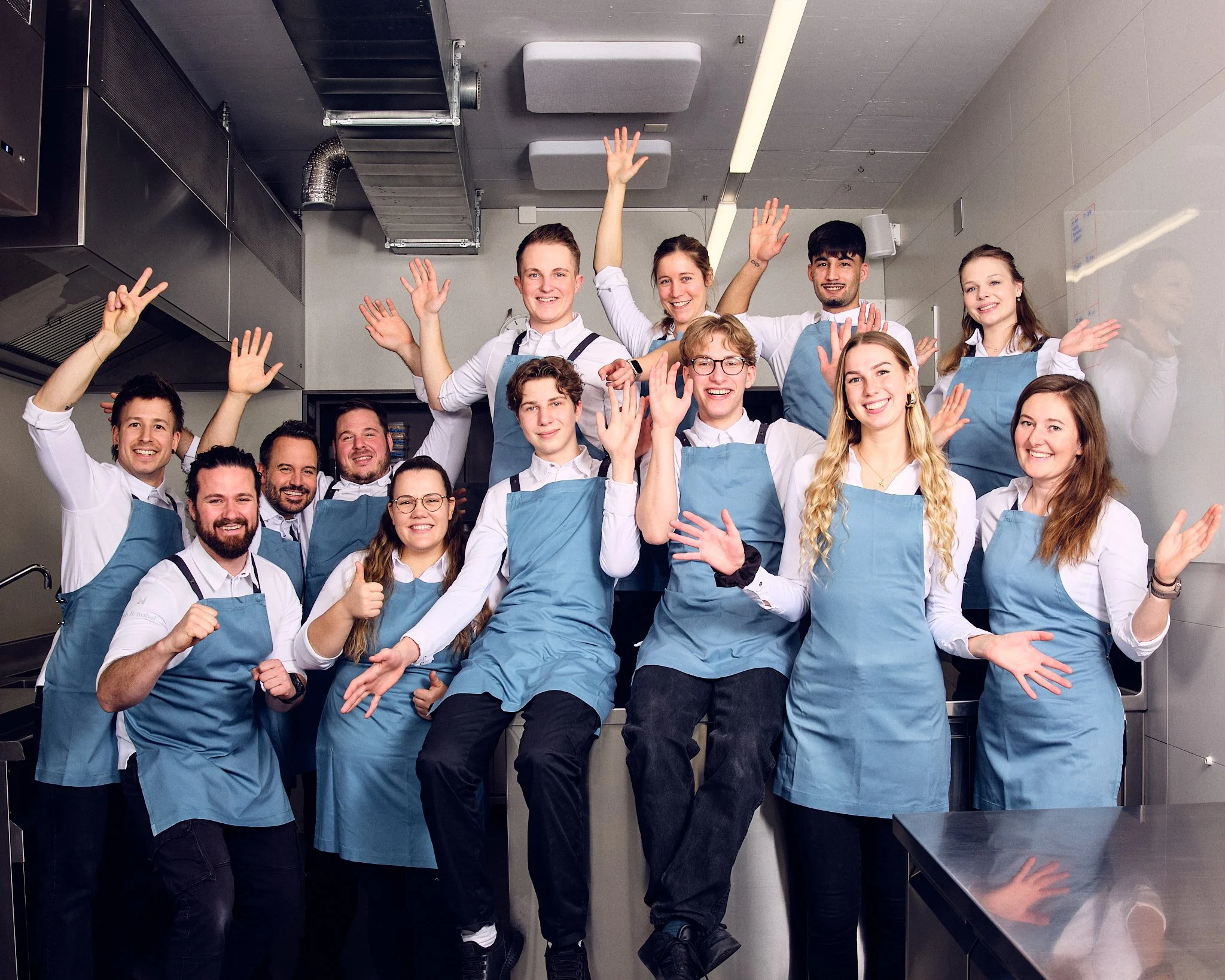 Fröhliche Menschen in Küchenuniformen feiern zusammen, einige winken und lachen.