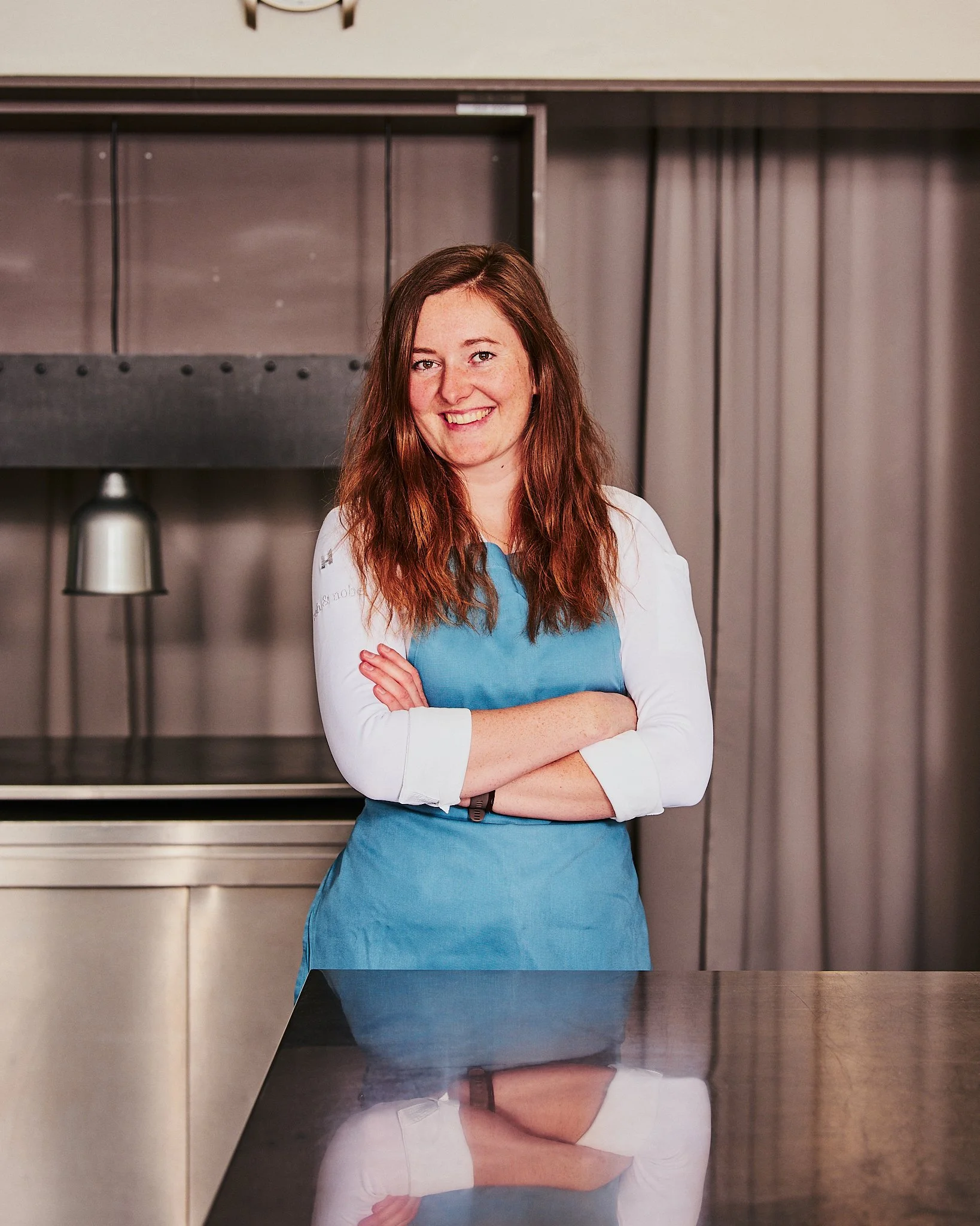 Eine Frau steht vor einer Kücheninsel mit verschränkten Armen und lächelt in die Kamera.