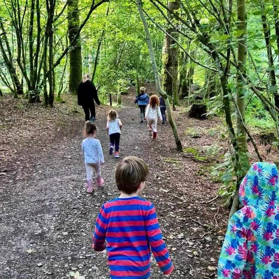 Children and an adult walking on a dirt trail in a lush, green forest.