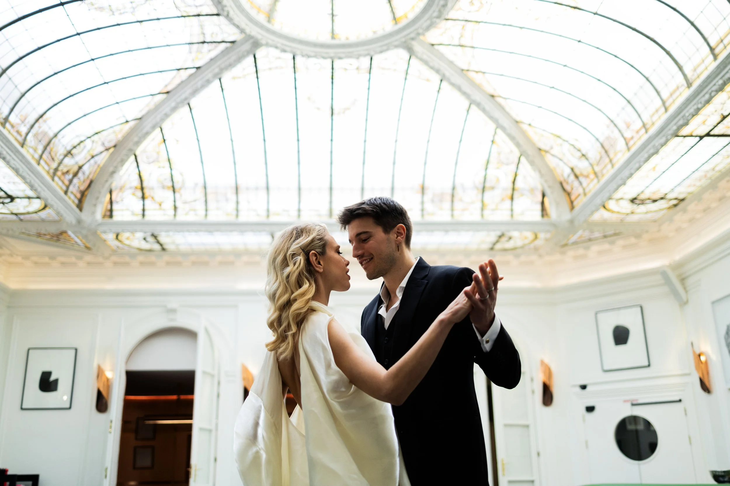 A couple dancing closely inside a grand room with a stained glass ceiling.