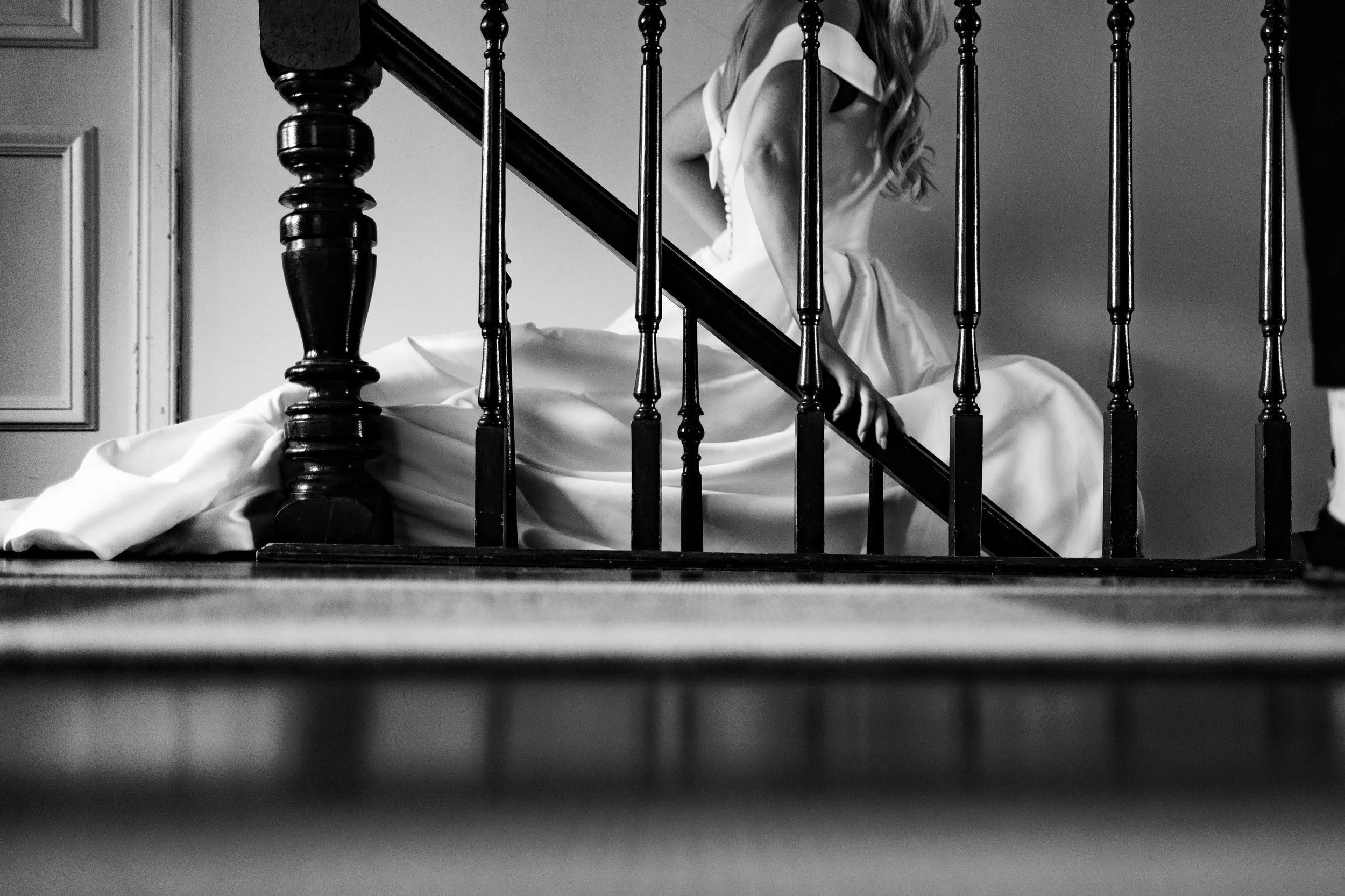 A woman descending a staircase on her wedding day, dressed in a wedding gown, with a person standing at the top of the stairs.