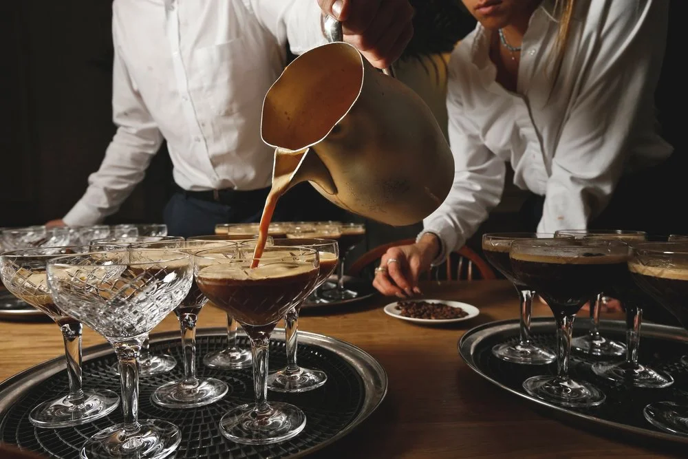 Bartender pouring espresso martini into cocktail glasses on a tray