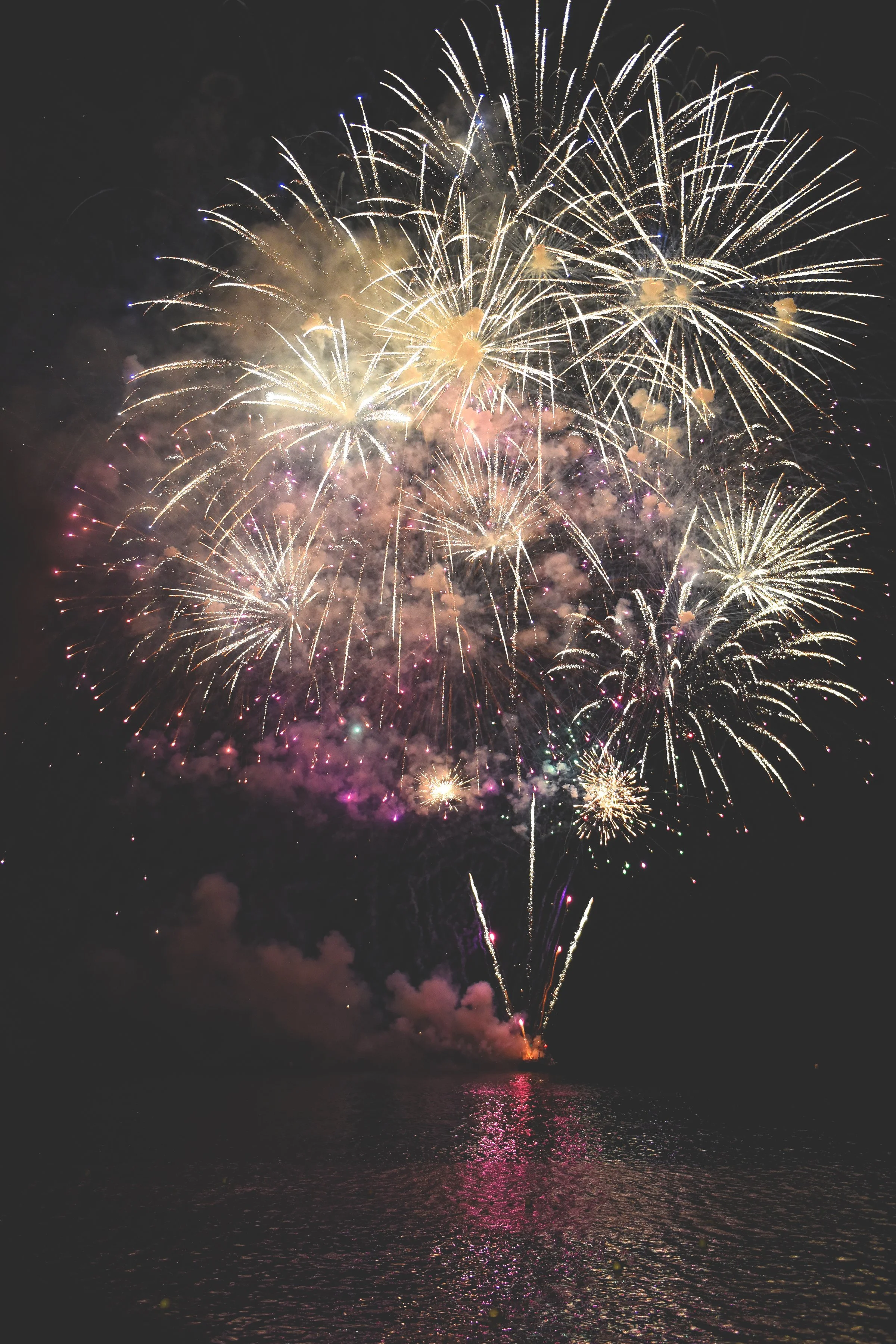 Colorful fireworks exploding in the night sky over a body of water.