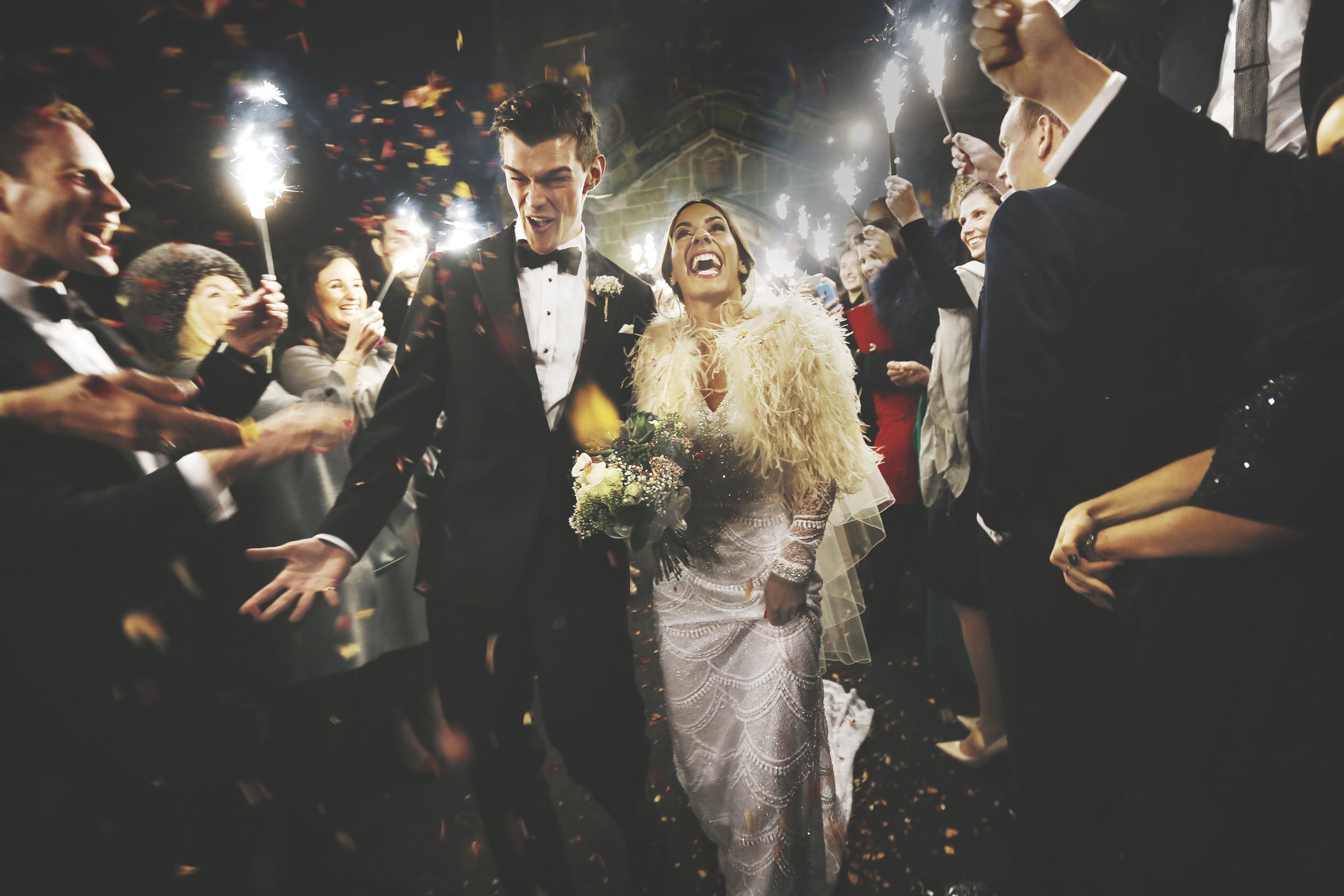 A bride and groom celebrating their wedding surrounded by friends holding sparklers at night.