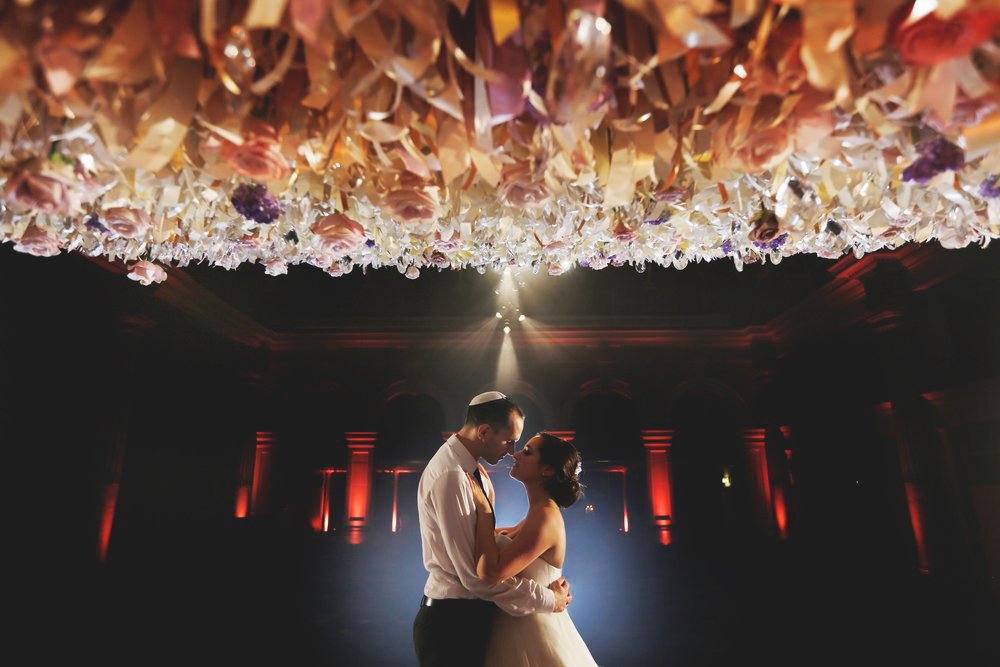 A couple dancing under a decorative ceiling during a wedding, with romantic lighting.