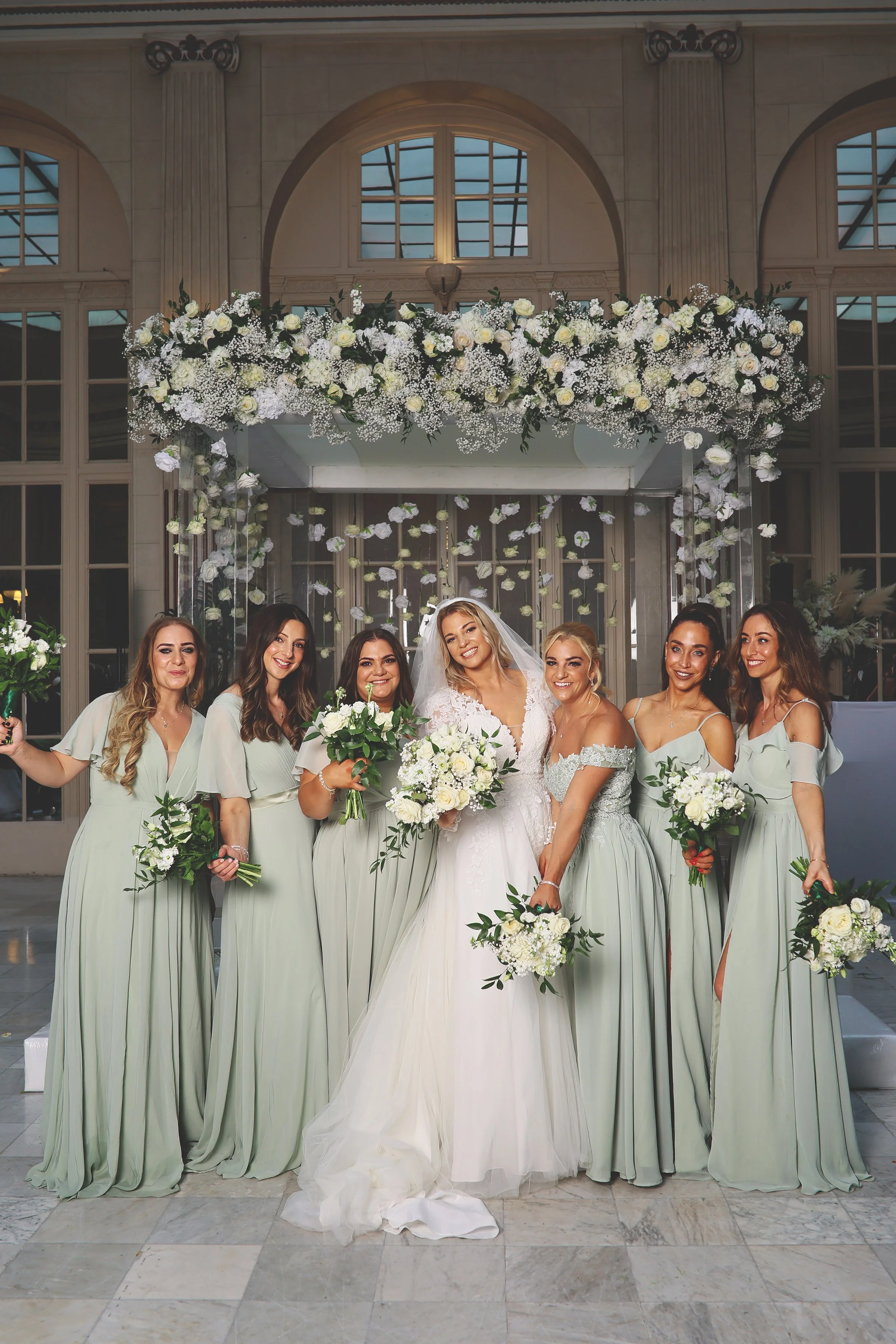 Bride with bridesmaids wearing light blue dresses holding bouquets in a wedding venue with floral decorations.