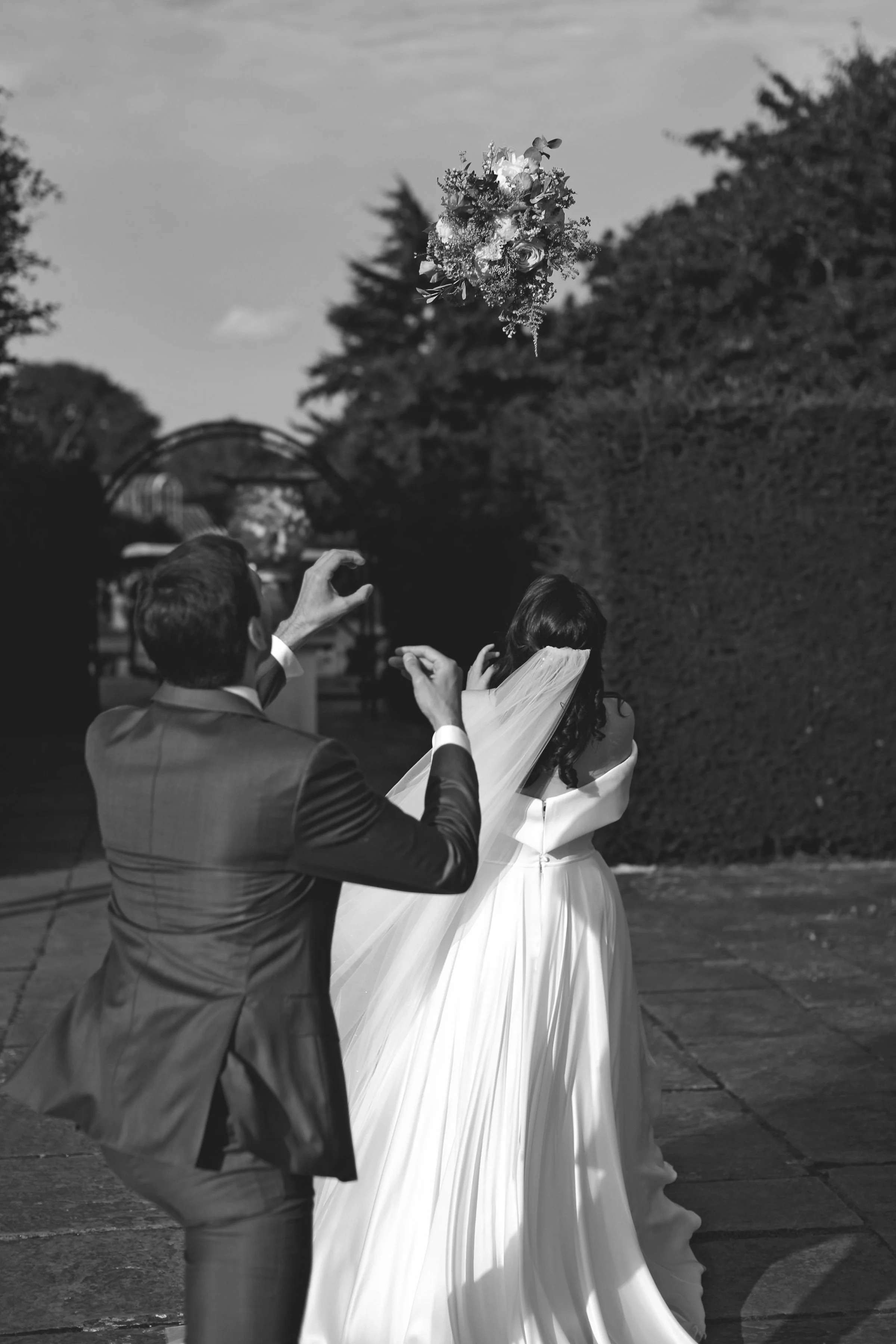Bride and groom watching bouquet toss at outdoor wedding in black and white
