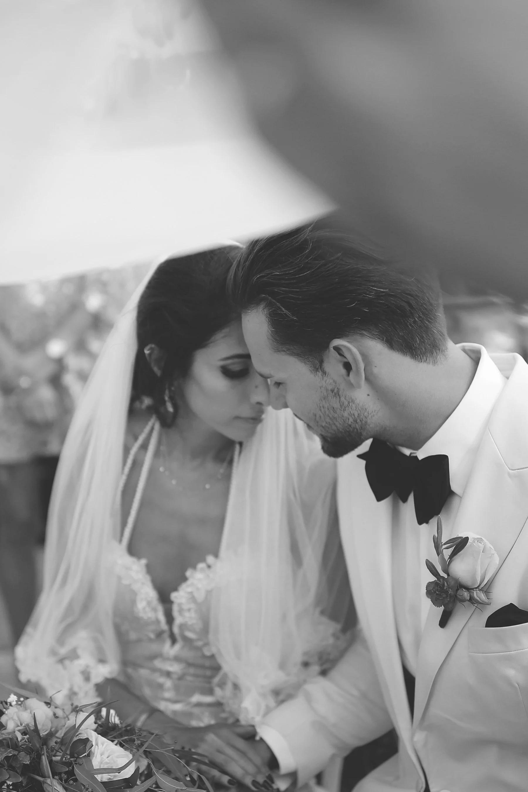 Bride and groom in intimate moment, black and white, wedding attire.