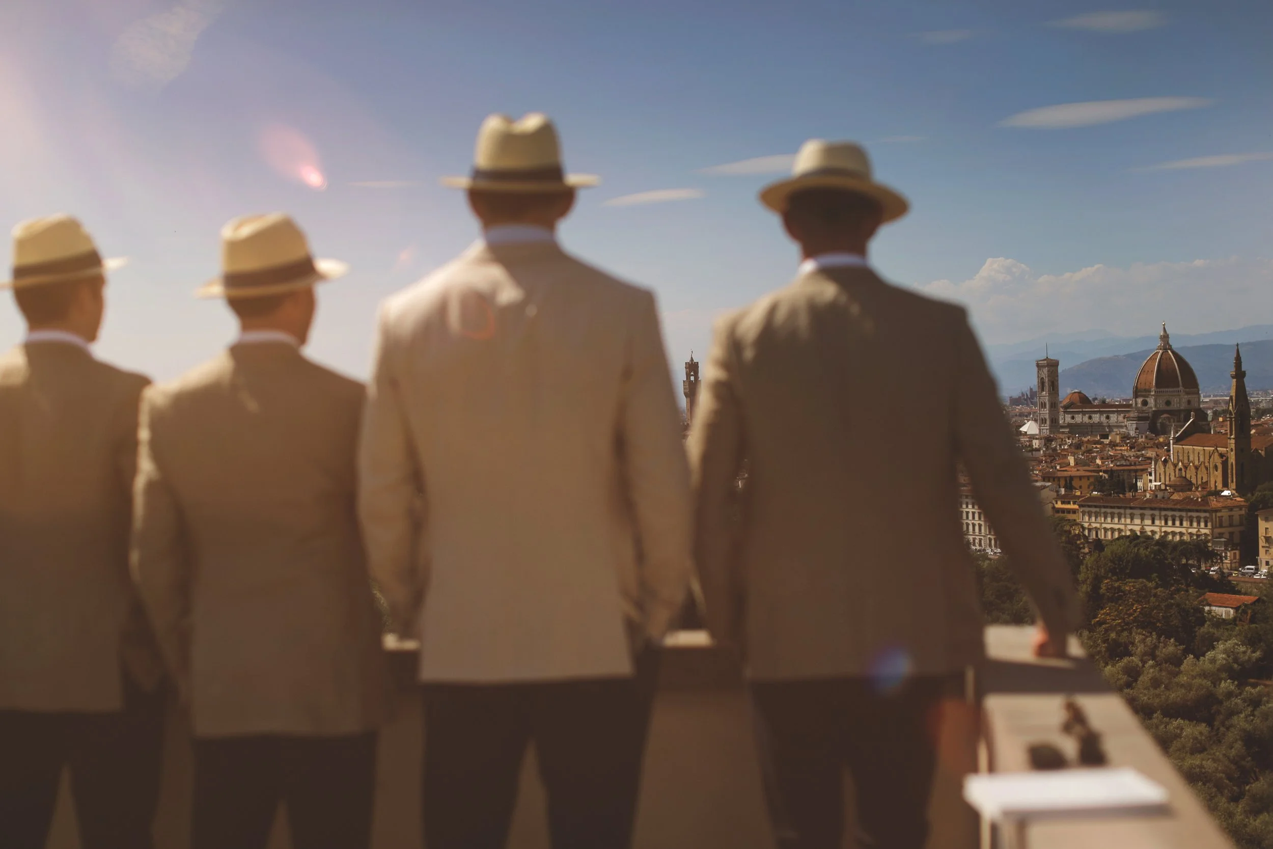 Four men in beige suits and hats facing a panoramic view of Florence, Italy, including the Florence Cathedral and skyline.