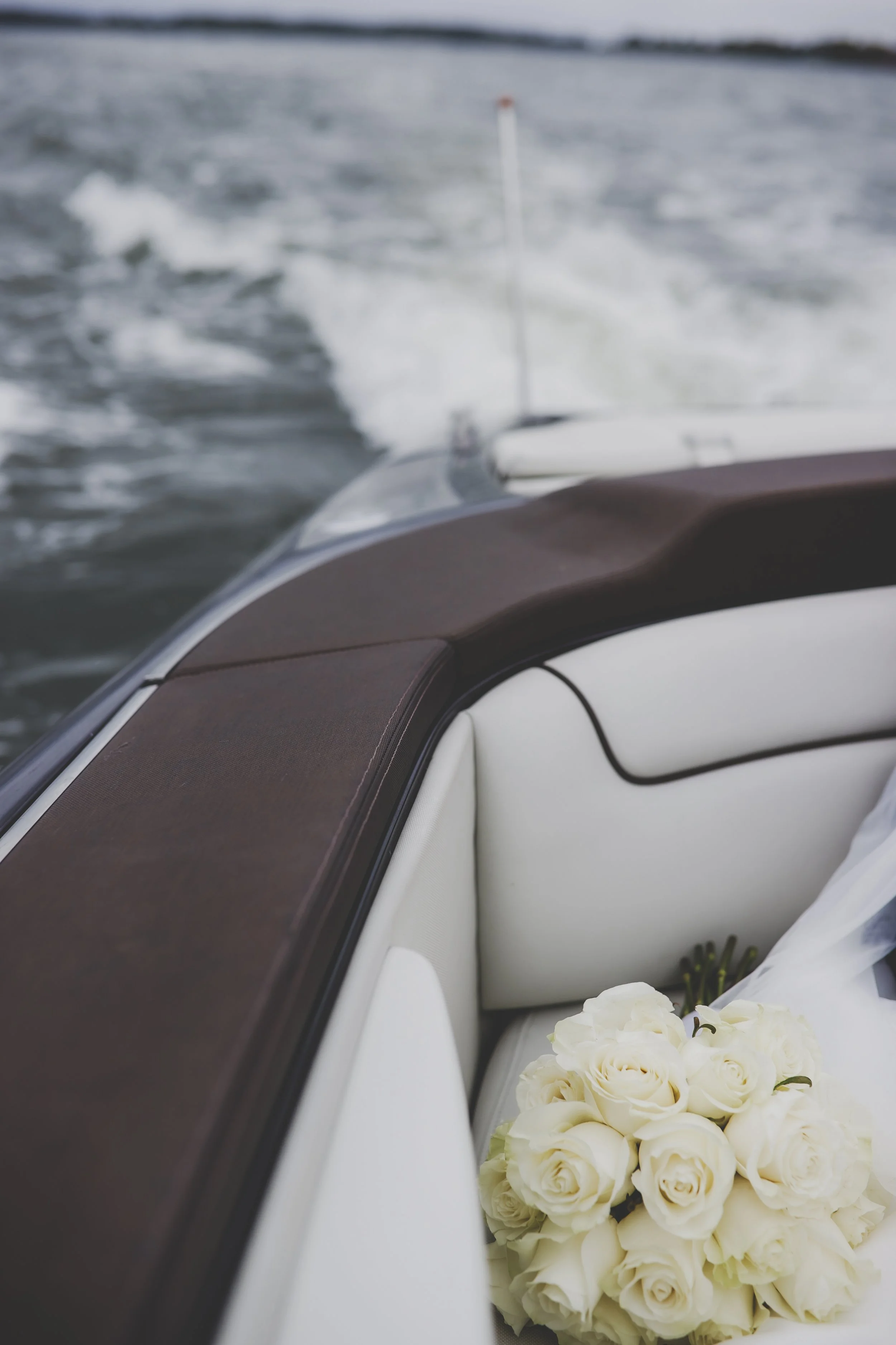 Close-up of a boat's interior with white leather seats, a dark brown wooden trim, and a bouquet of white roses.