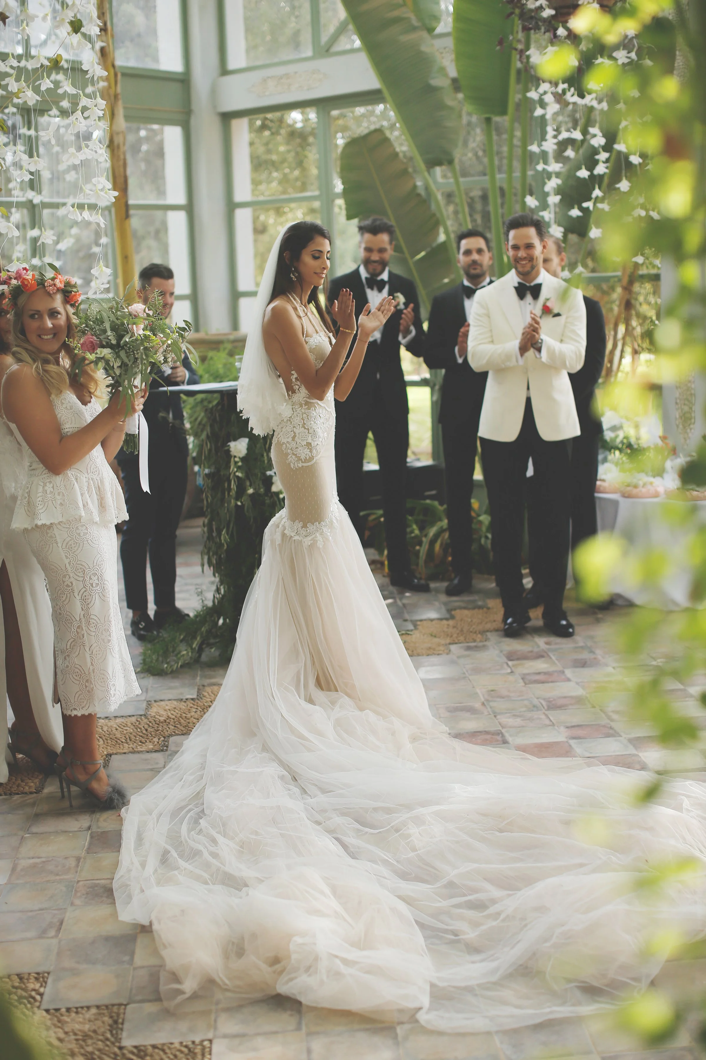 Bride in wedding dress clapping with guests in greenhouse ceremony