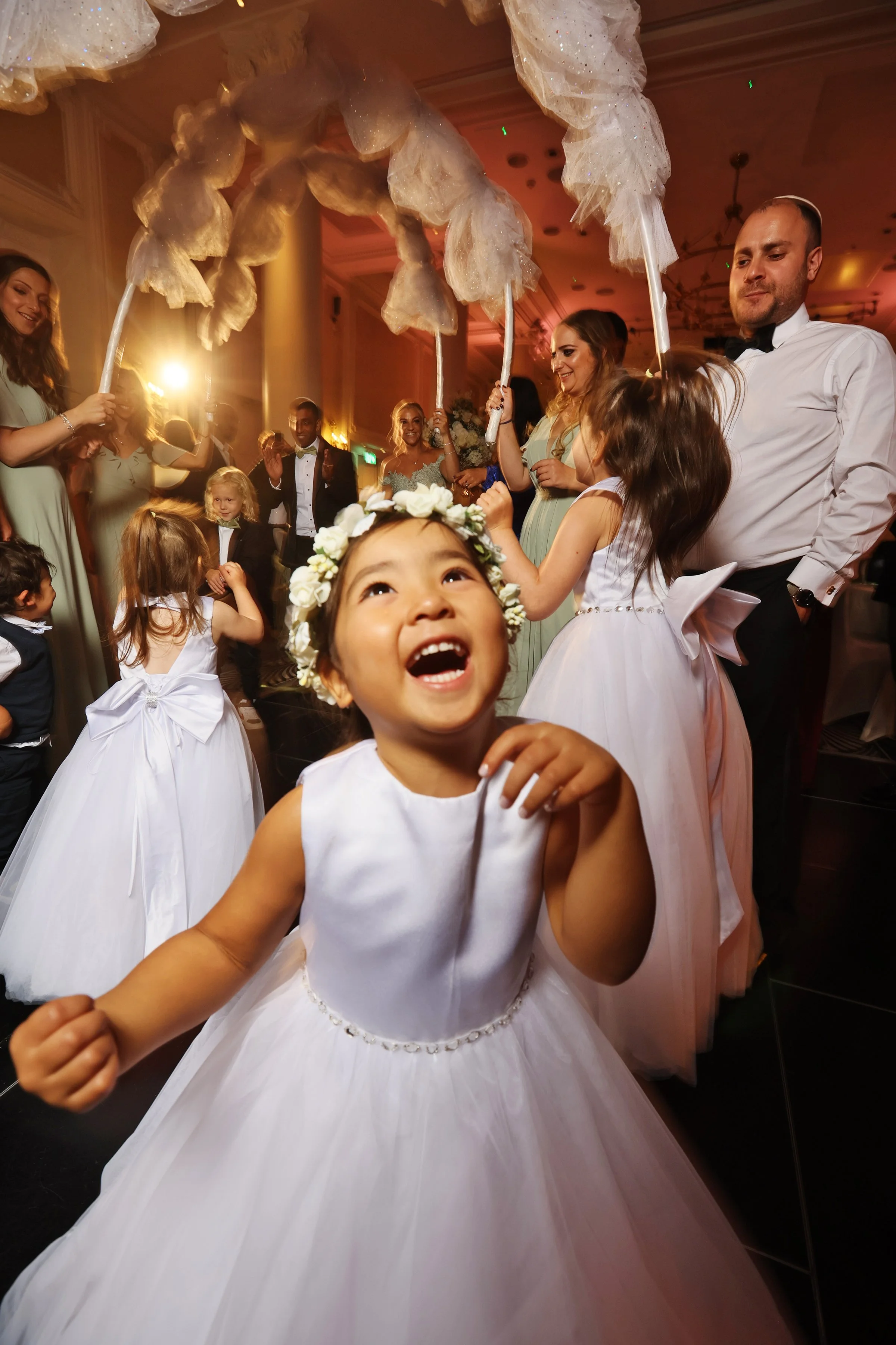 Children and adults celebrating at a wedding reception, with children dressed as flower girls and holding large white cotton candy on sticks.