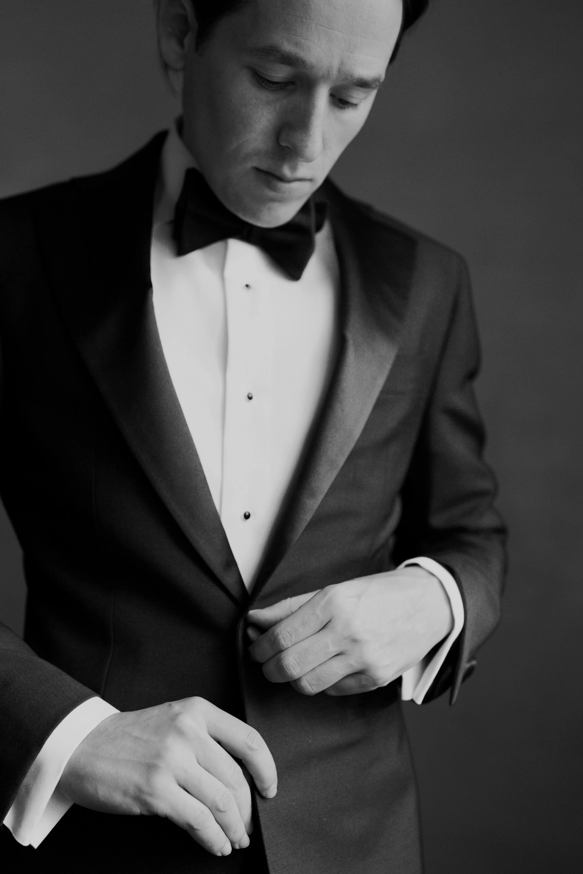 Black and white photo of a man in a tuxedo adjusting his sleeve.