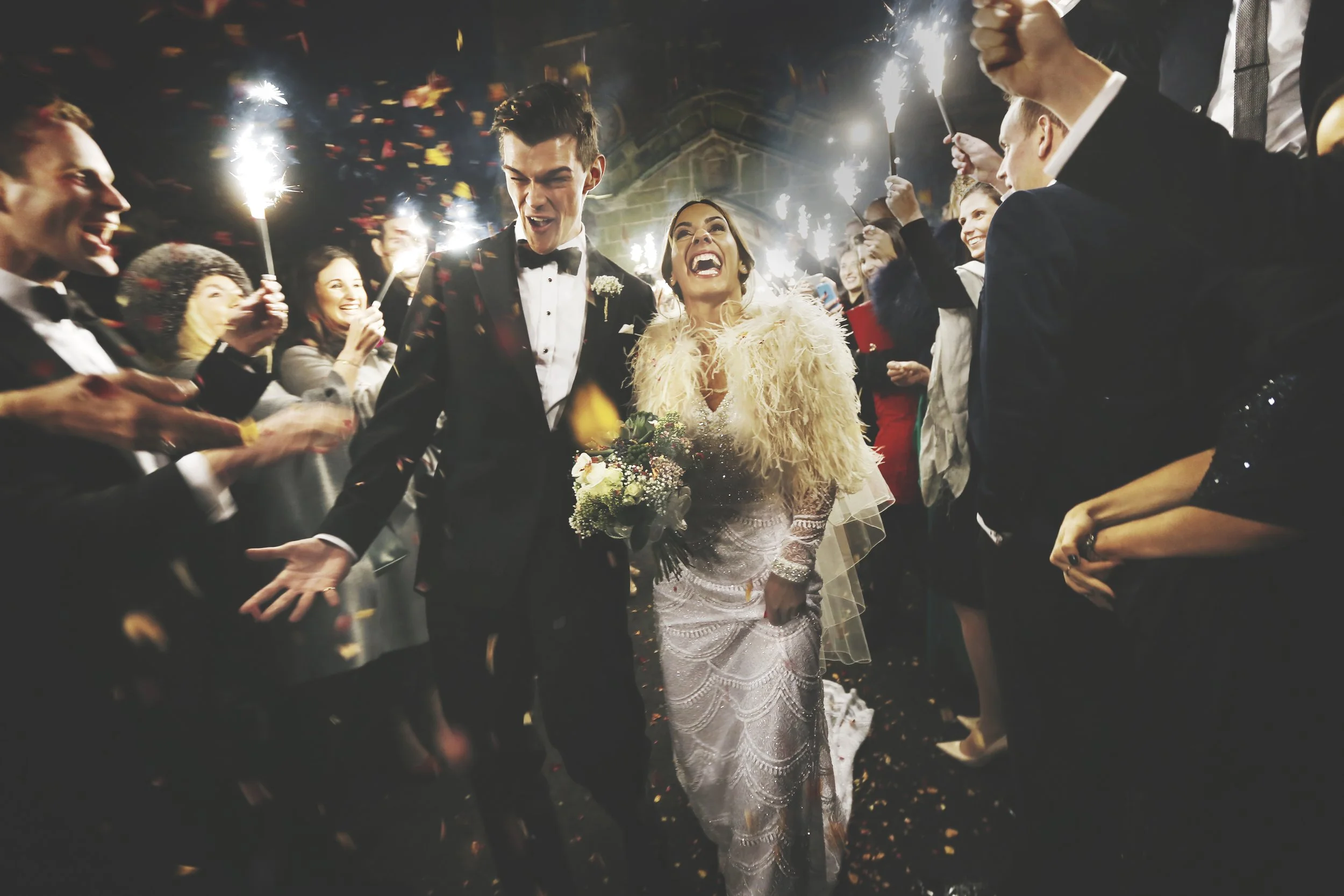 A bride and groom celebrating their wedding surrounded by friends holding sparklers at night.