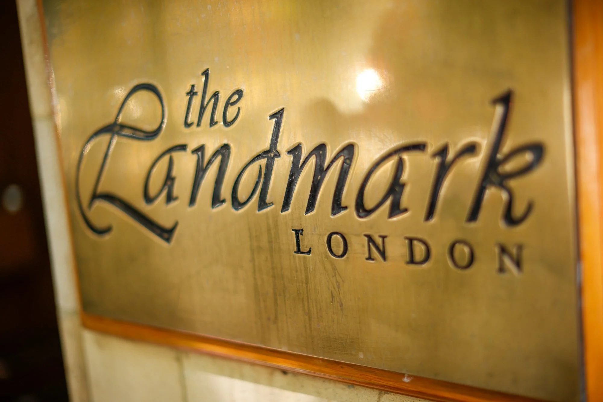 Close-up of a metallic sign with engraved and painted text reading 'the Landmark' and 'LONDON' beneath, possibly part of a hotel's or landmark's nameplate.