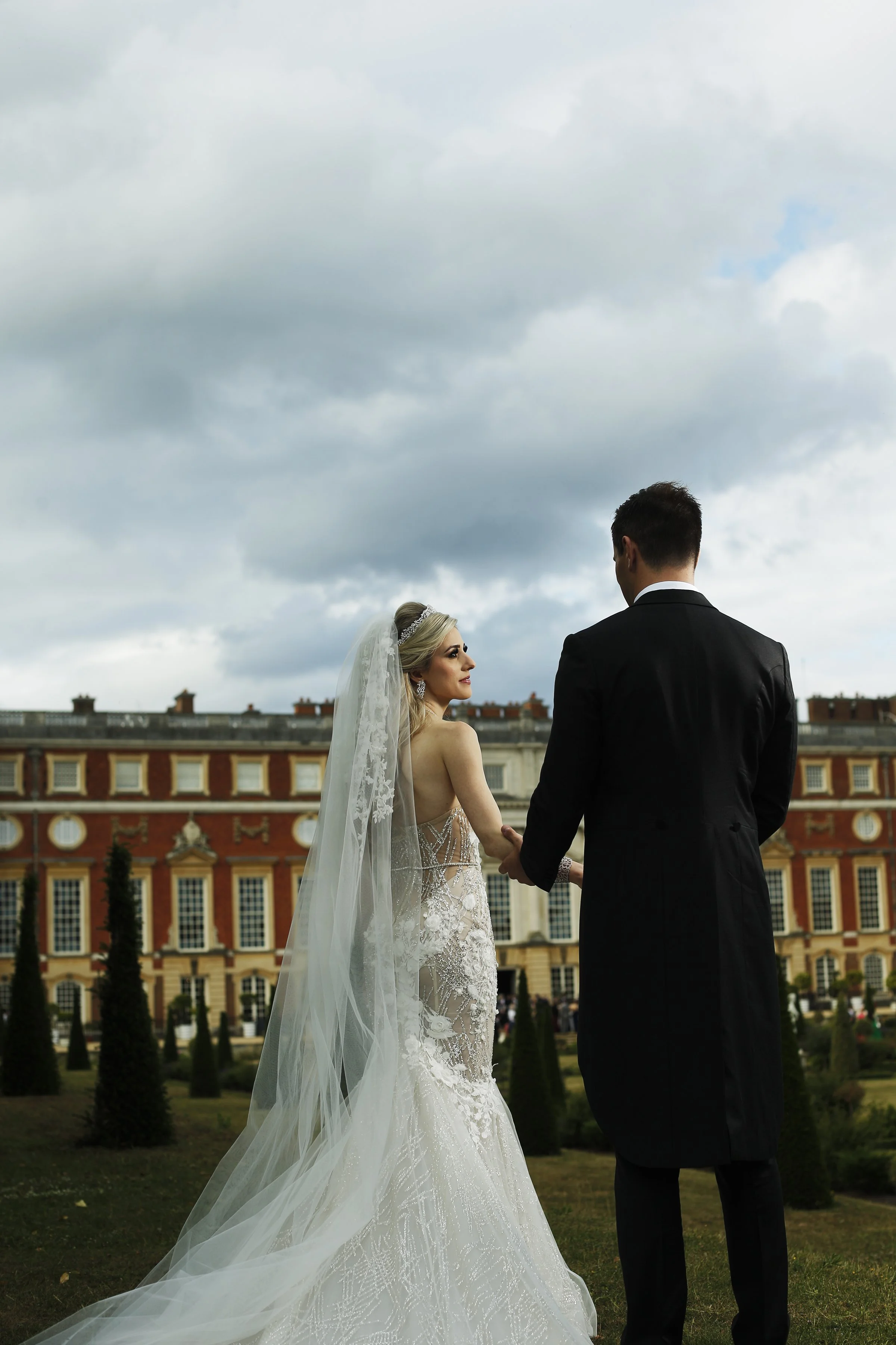 Bride and groom holding hands, looking out toward Hampton Court Palace