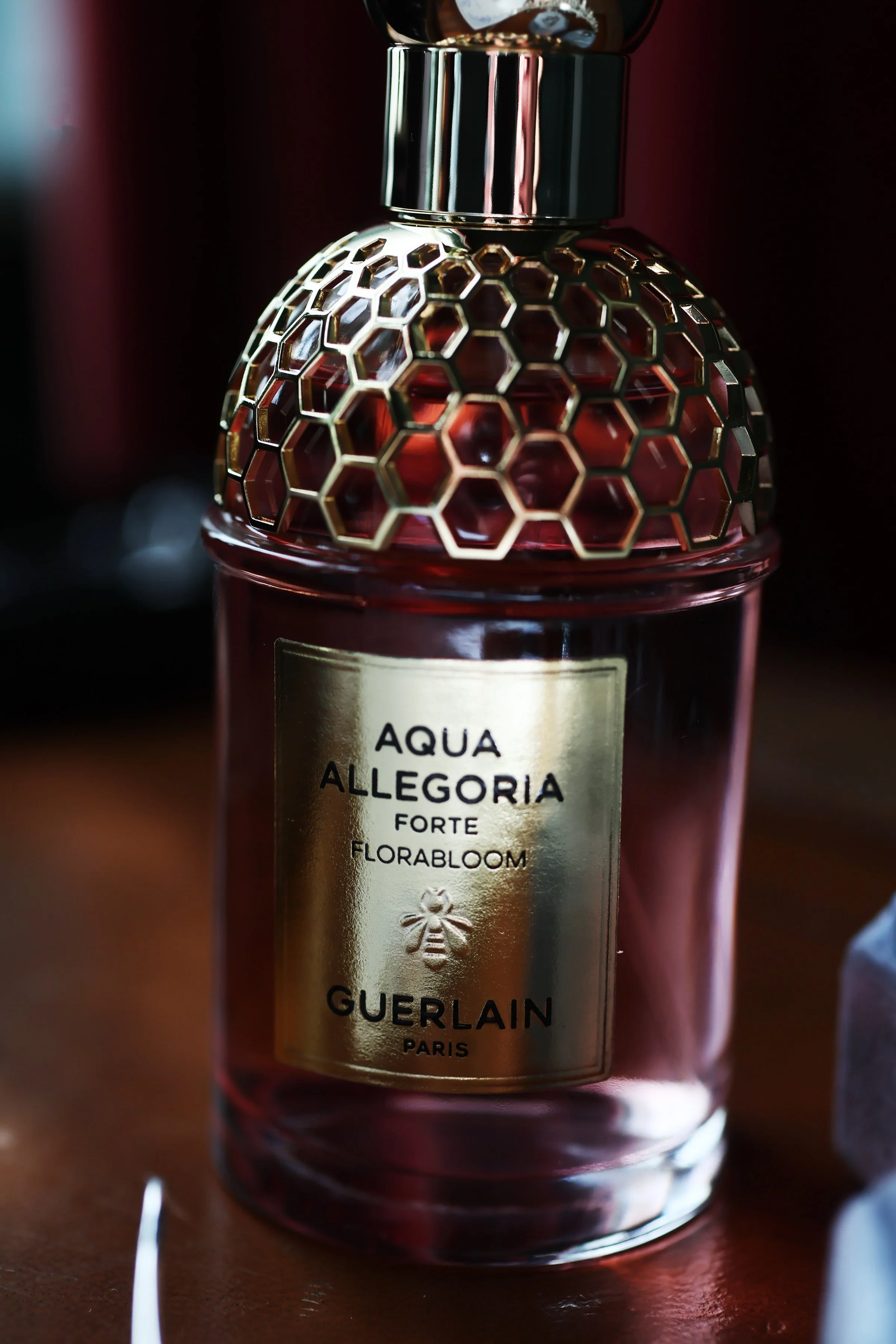 A perfume bottle with a gold honeycomb cap and label reading 'Aqua Allegoria Forte Florabloom by Guerlain Paris, featuring a bee icon.