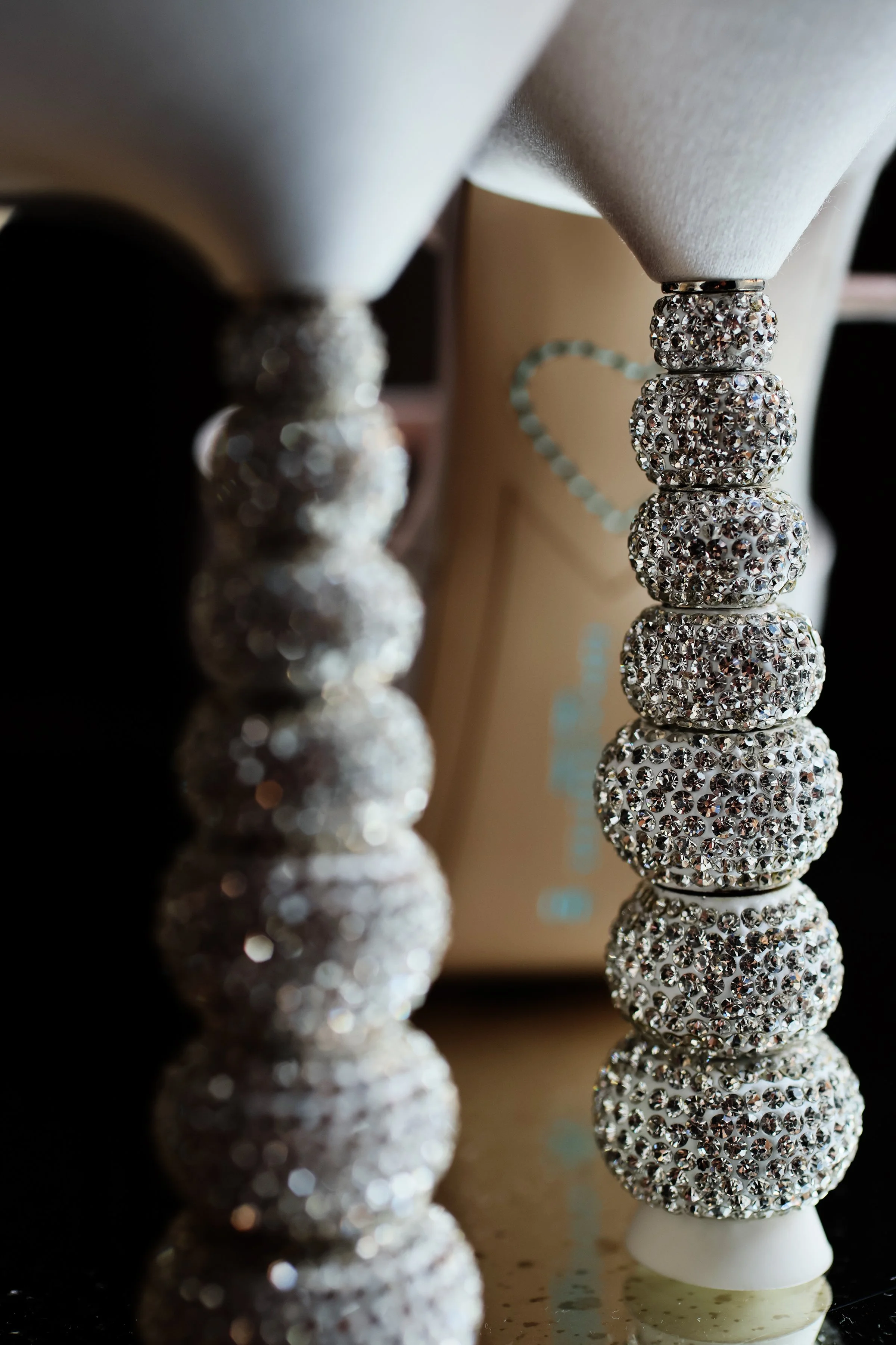 A close-up view of a decorative object made of stacked, spherical, rhinestone-covered beads on a white base, with a mirror reflection showing on a glossy surface.