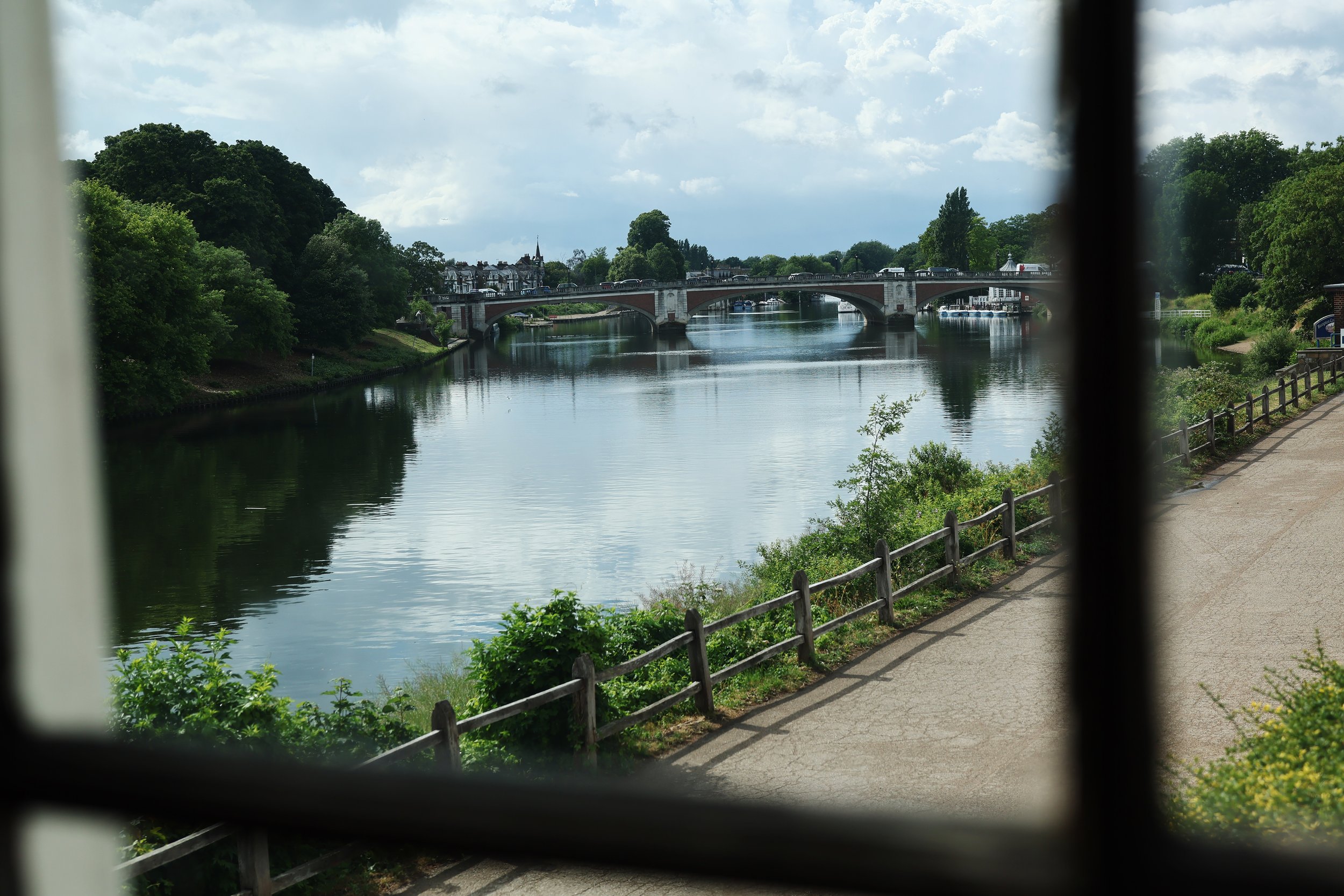 View of a river with a bridge, surrounded by green trees and buildings in the distance, taken through window bars.
