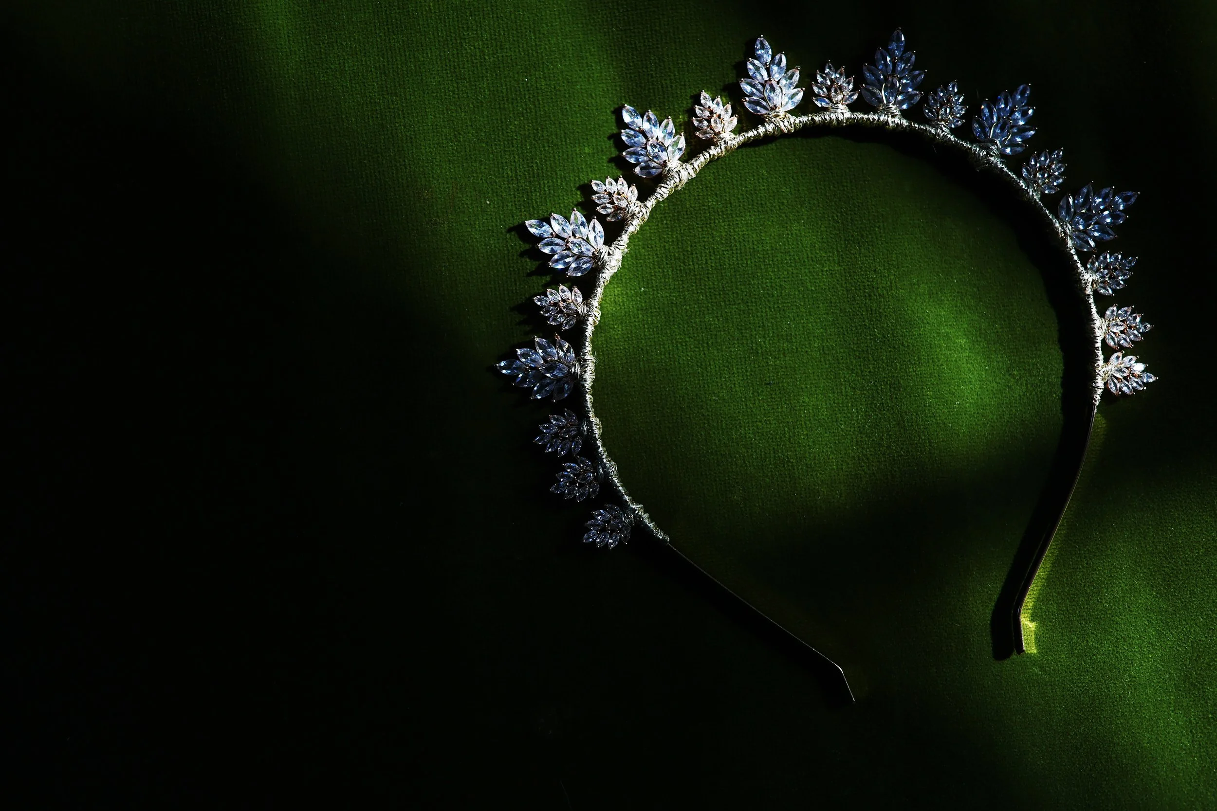 A silver tiara with leaf-shaped clear gemstones, resting on a green fabric surface.