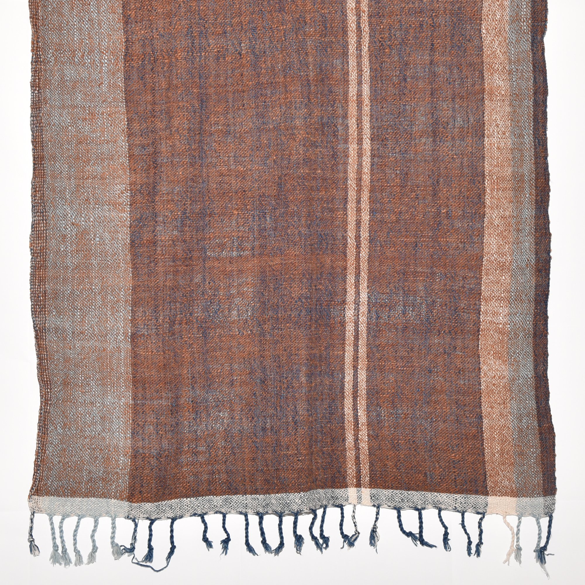 A luxurious, hand-woven shawl made from thick organic cotton. Featuring bold stripes in brown, tan, indigo, and white, it's finished with tassels.
