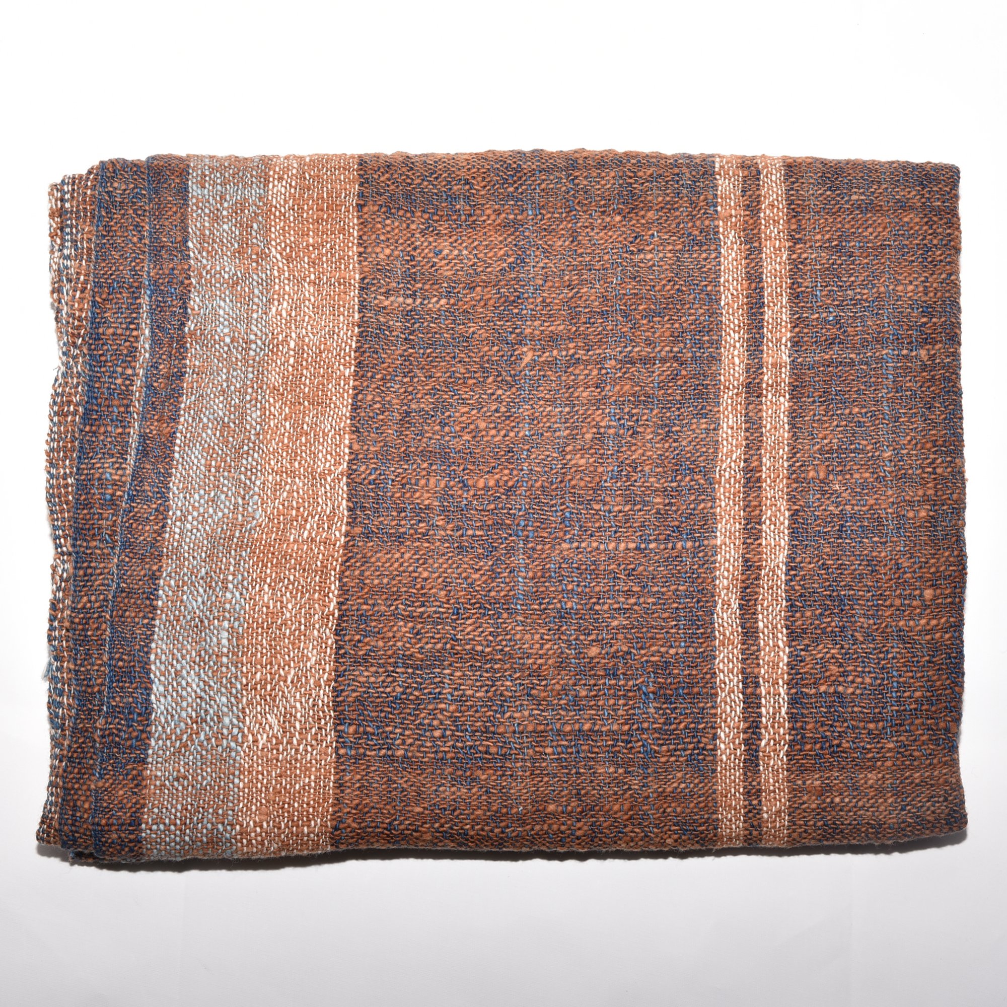 A luxurious, hand-woven shawl made from thick organic cotton. Featuring bold stripes in brown, tan, indigo, and white, it's finished with tassels.