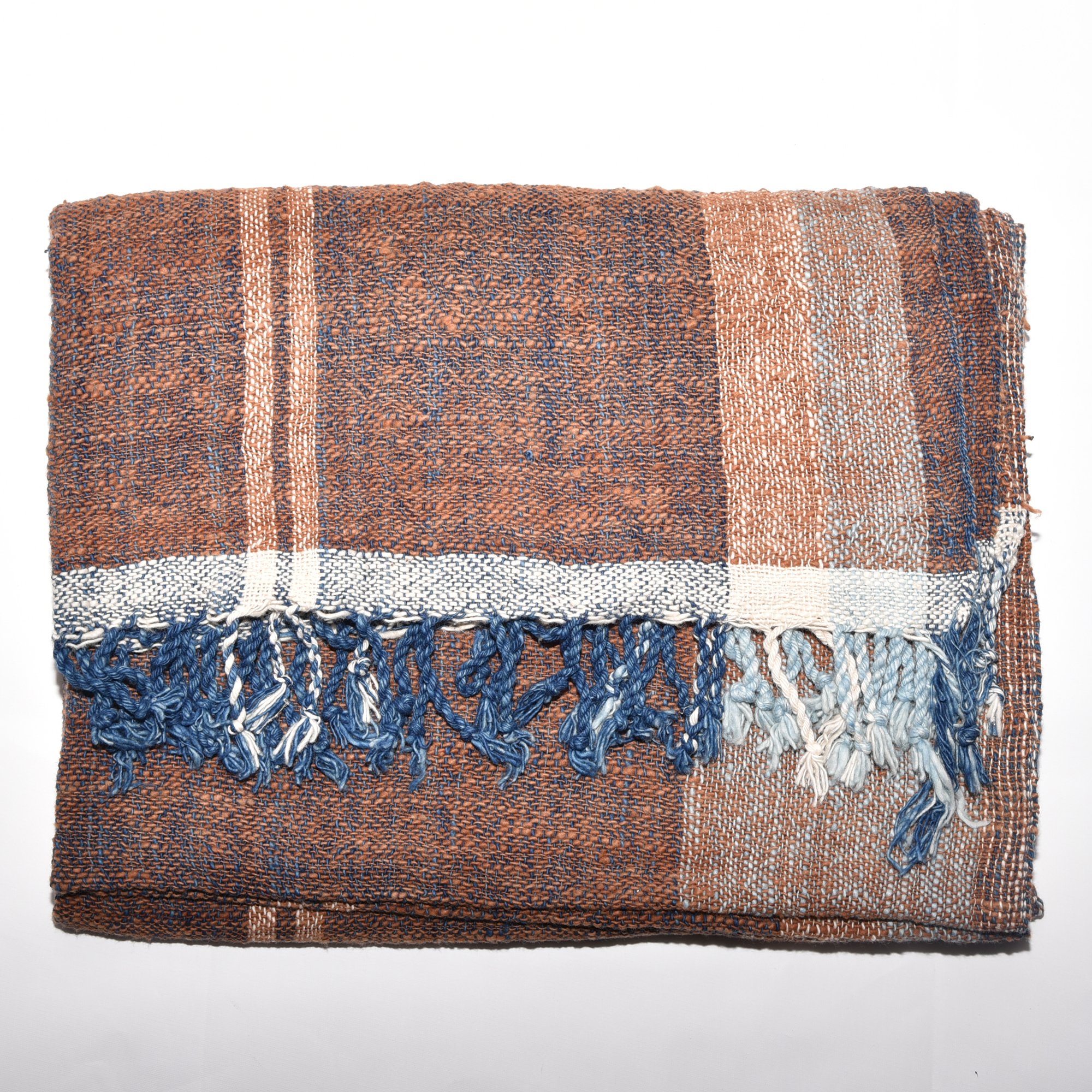 A luxurious, hand-woven shawl made from thick organic cotton. Featuring bold stripes in brown, tan, indigo, and white, it's finished with tassels.
