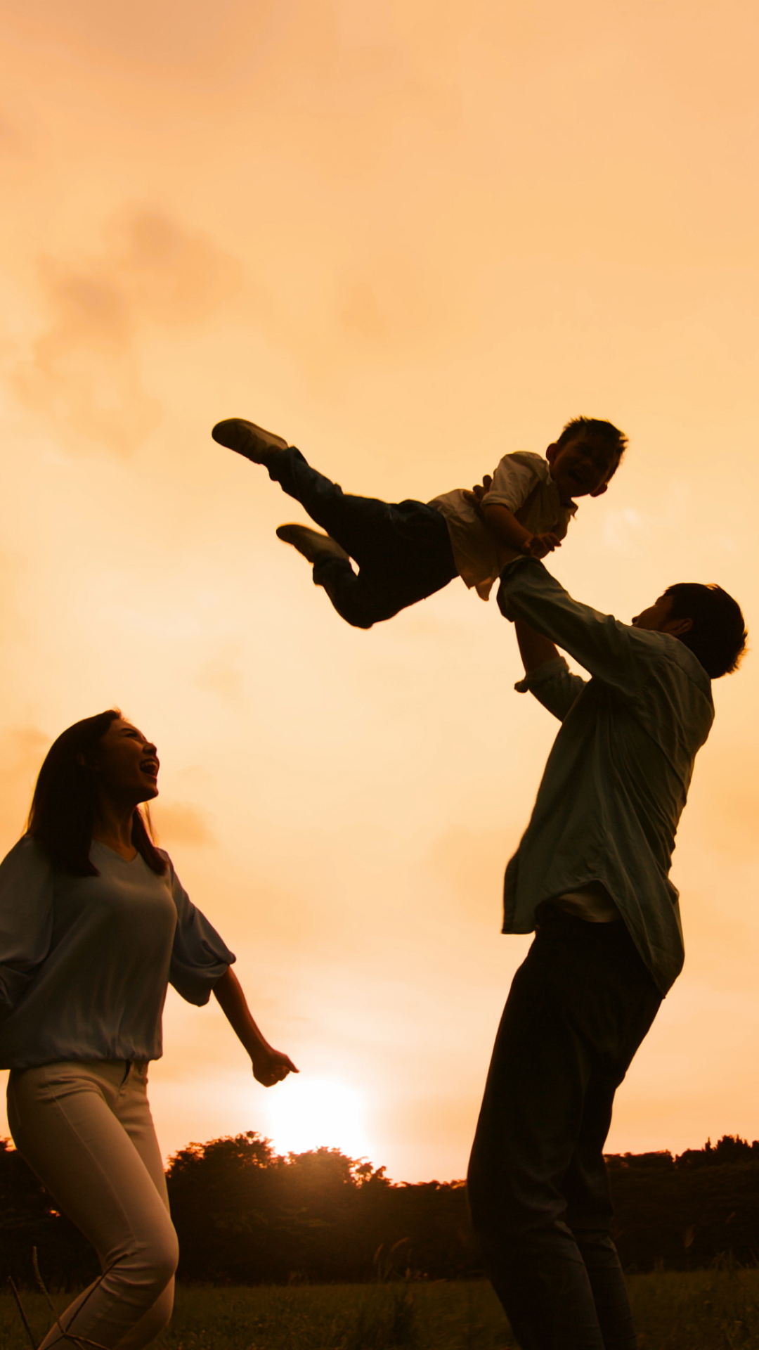 parents and child silhouette at sunset playing at the park