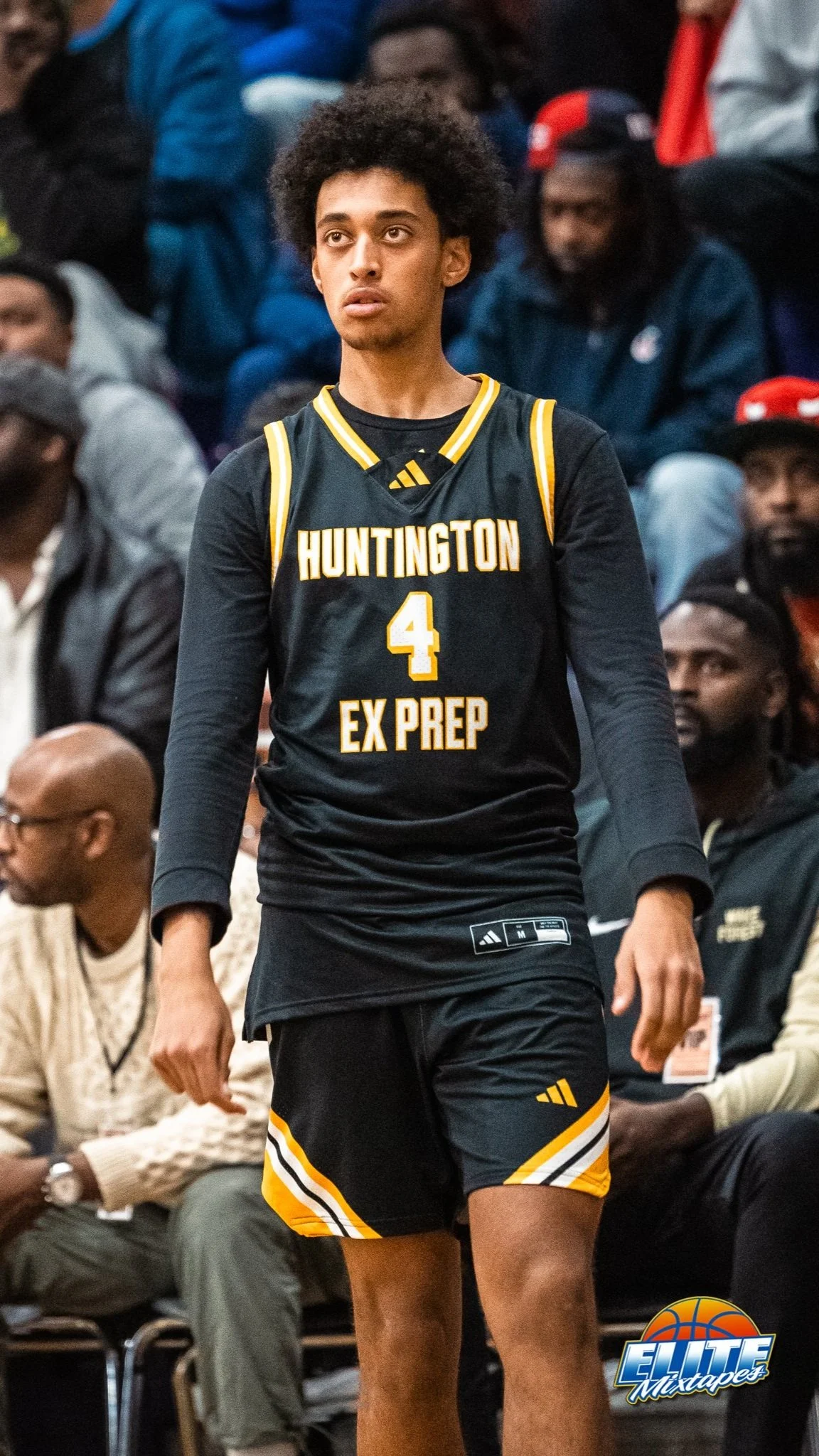 Een jonge man in een zwart basketbal jersey met gele details, nummer 4 en de tekst 'Huntington Ex Preps', staat tijdens een basketbalwedstrijd.