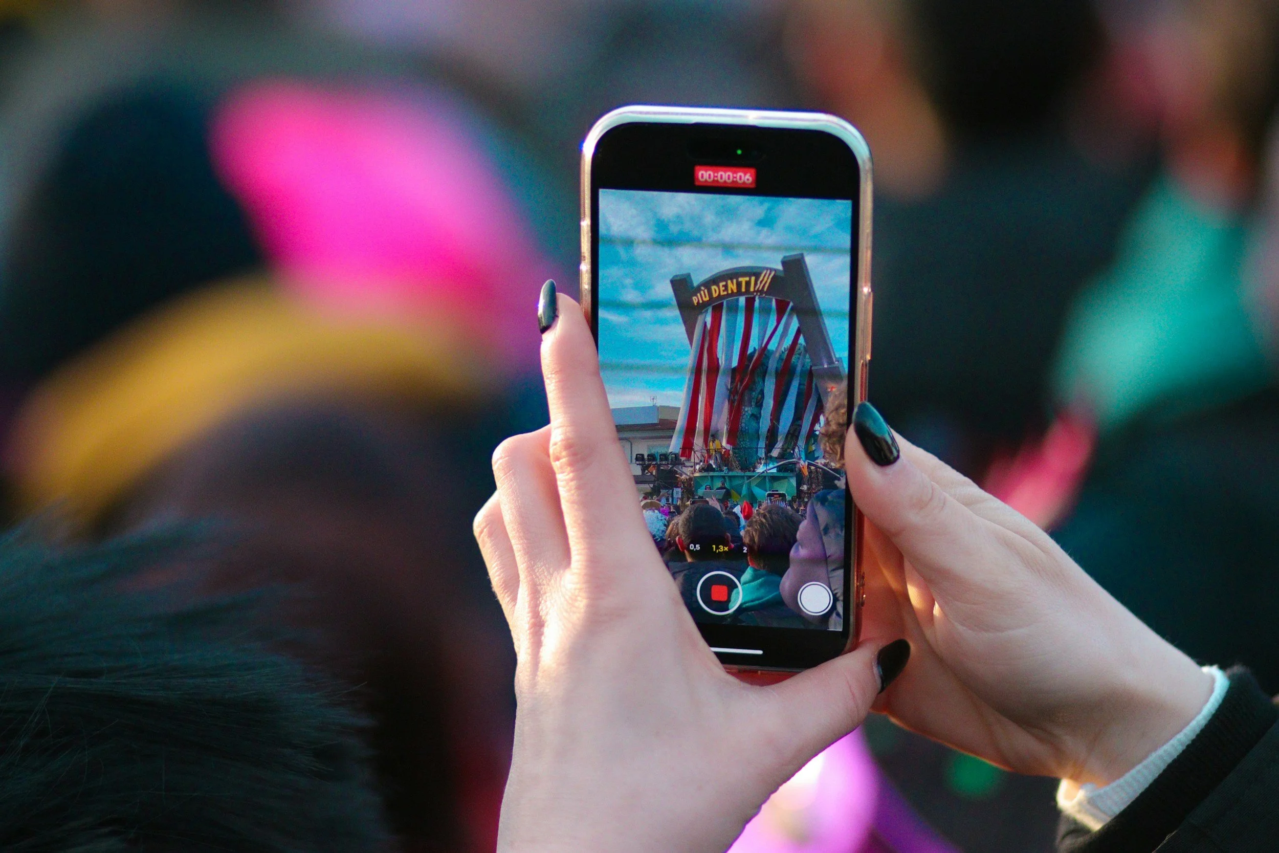 Person holding a smartphone recording a carnival or festival scene with a large colorful decoration and a crowd of people.