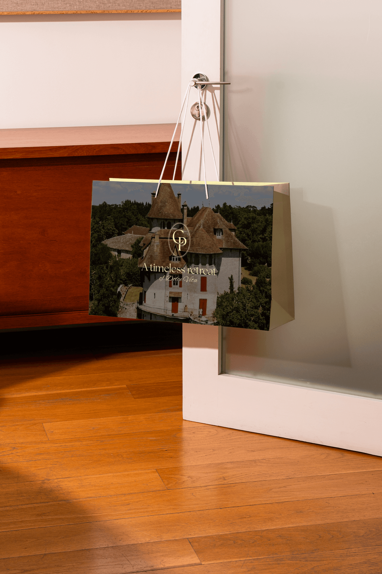 Sac en papier avec une photo d'une maison historique entourée d'arbres, suspendu à une porte dans un intérieur avec plancher en bois.