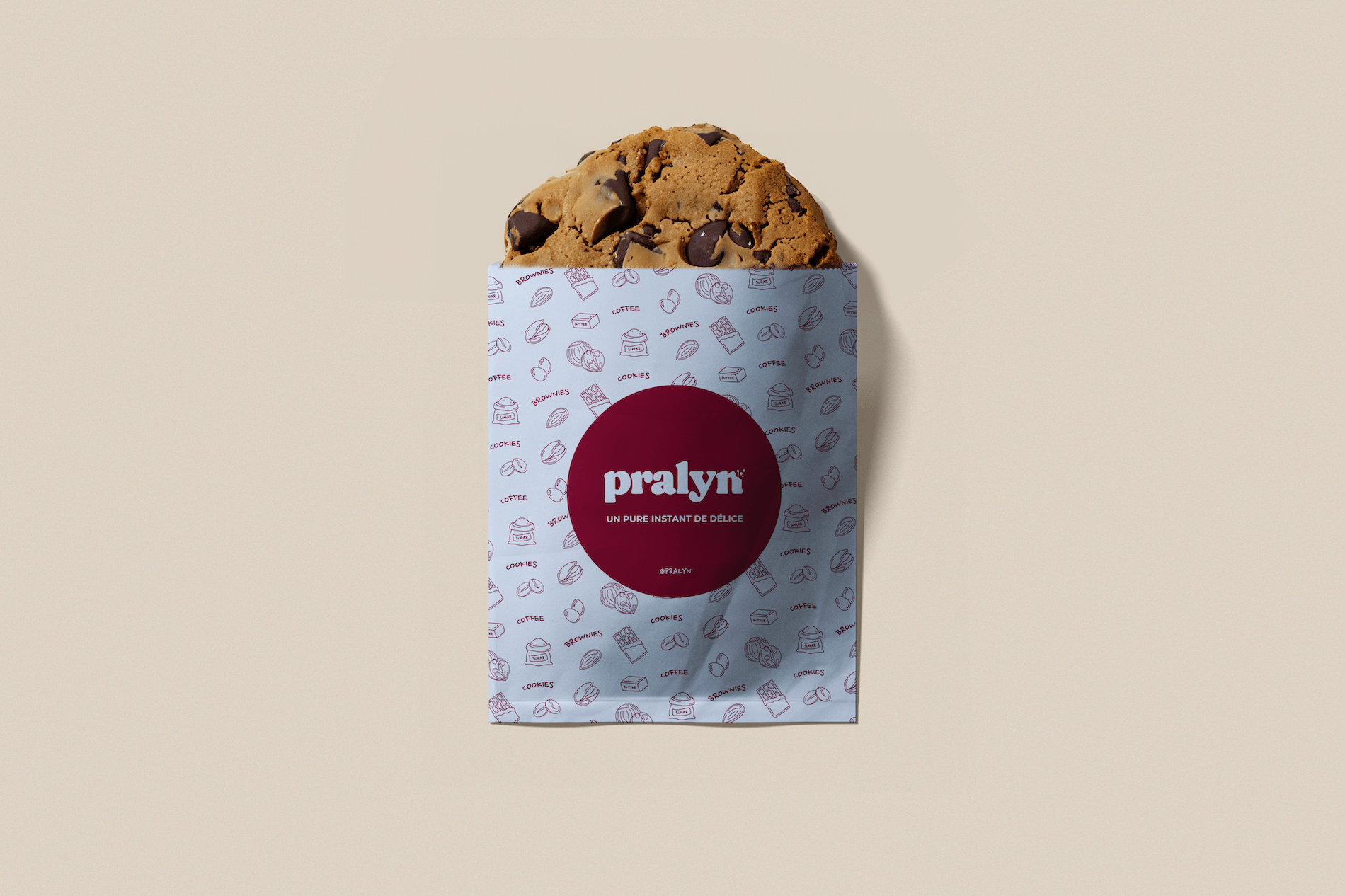 Un muffin aux pépites de chocolat dans un emballage de marque Pralyn. L'emballage est blanc avec des illustrations de biscuits, de café, de chocolat et autres snacks, et a un cercle rouge avec le texte "Pralyn, un pur instant de délice".
