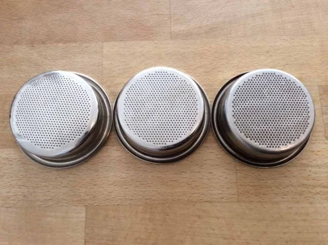 Three metal cupcake liners with perforated bottoms lined up on a wooden surface.