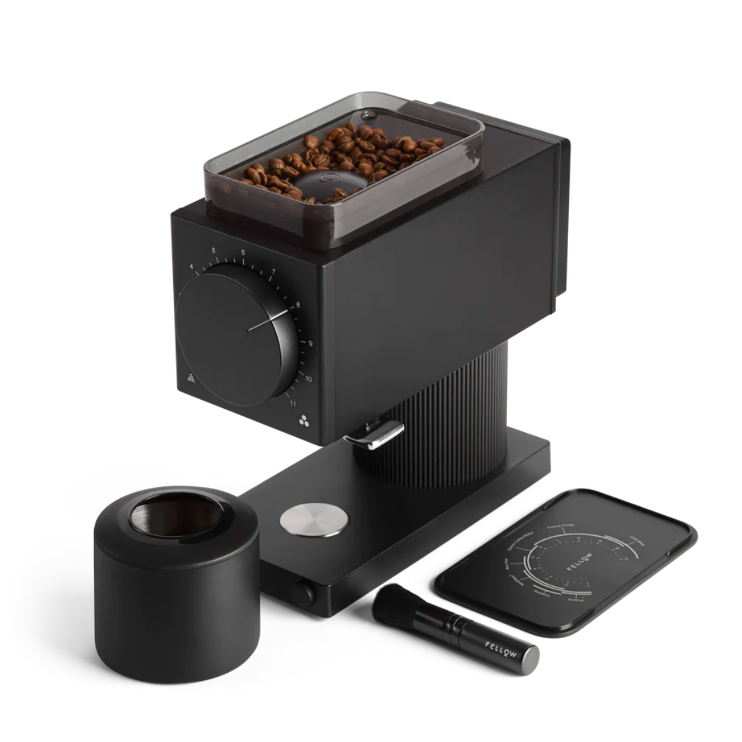 Black coffee grinder with beans, tamping tool, cleaning brush, and a smartphone with a coffee app, all on a white background.