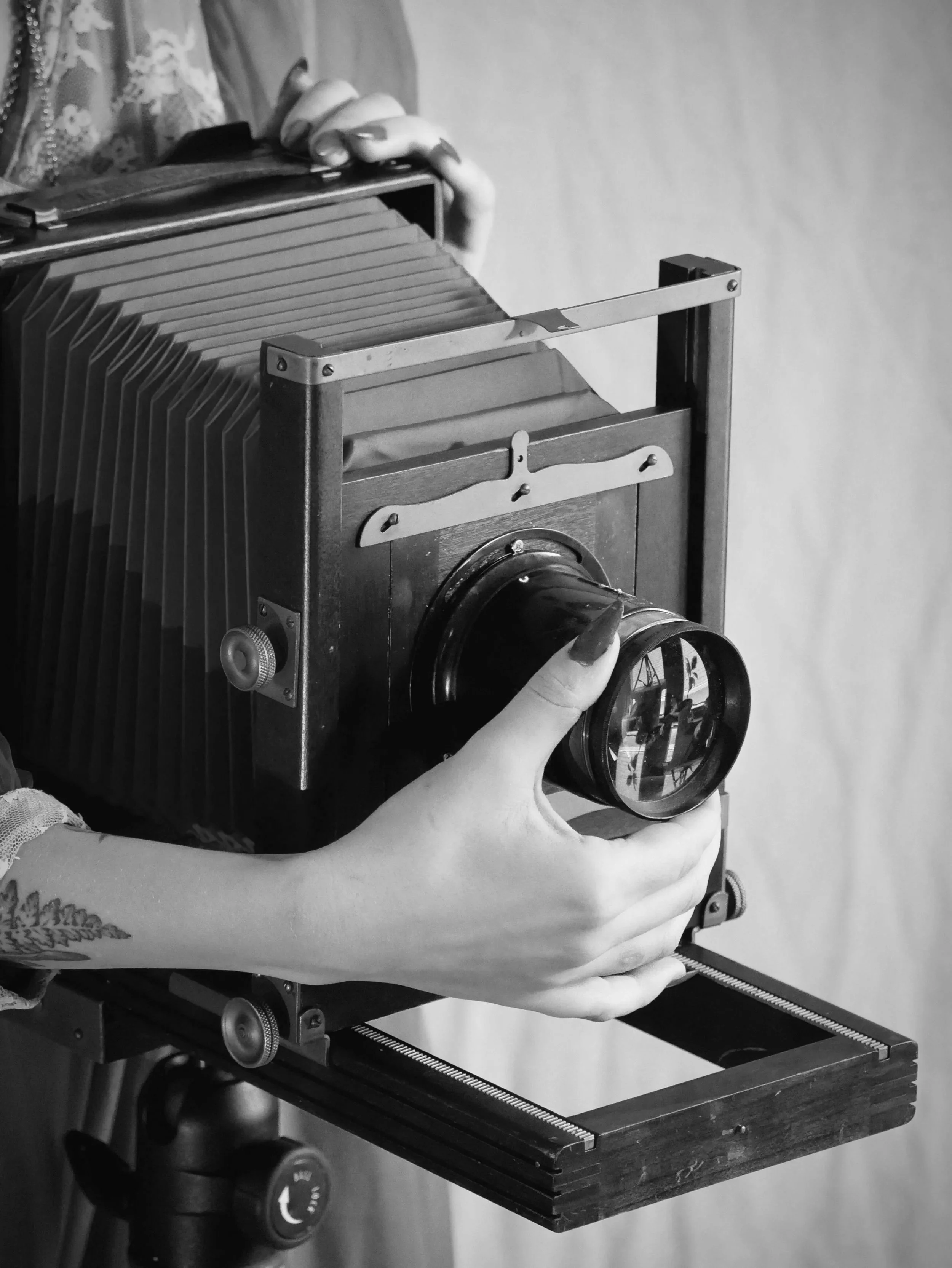 A person holding a vintage large format camera with a wooden base and bellows, preparing for photography.