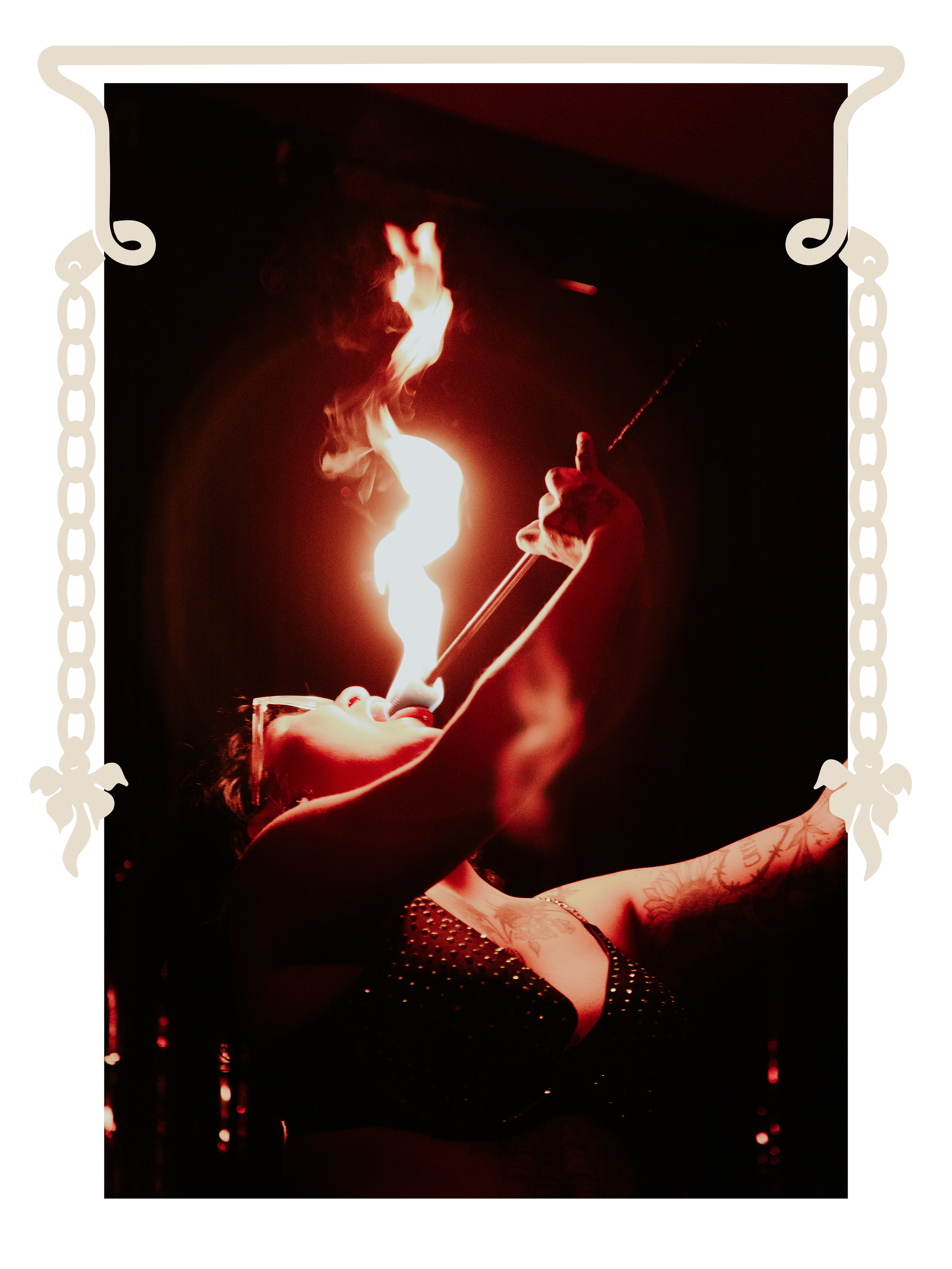 A woman with tattoos on her arm is performing a fire-eating act, holding a flaming object near her mouth in a dark setting with red lighting.