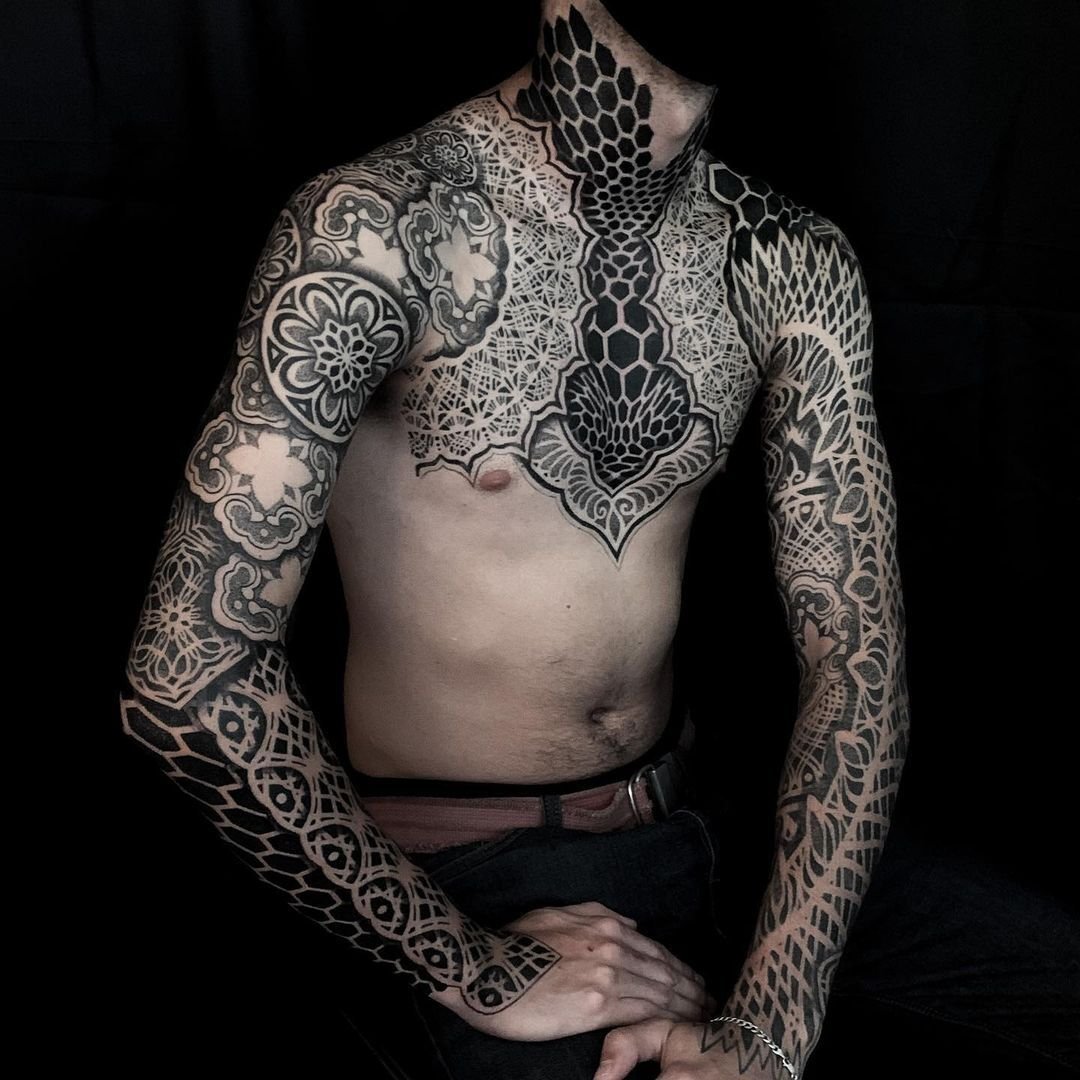 intricate black ink tattoos covering chest and arms, blackwork, ornamental