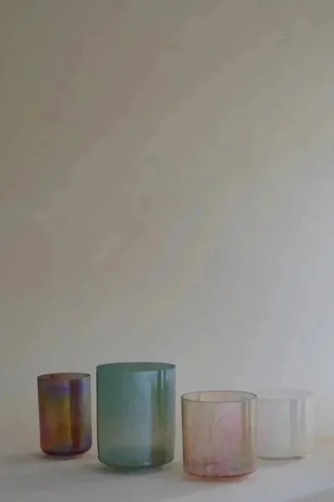 Quatre verres en verre coloré de différentes tailles alignés sur une surface blanche, avec un fond neutre.