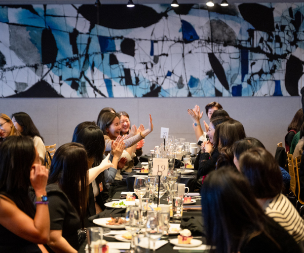 A group of people sitting at long banquet tables, celebrating with high-fives and smiles in a formal event setting.