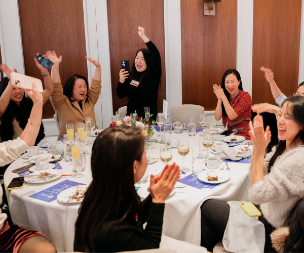 Group of women celebrating at a dining table with drinks, clapping, and cheering.