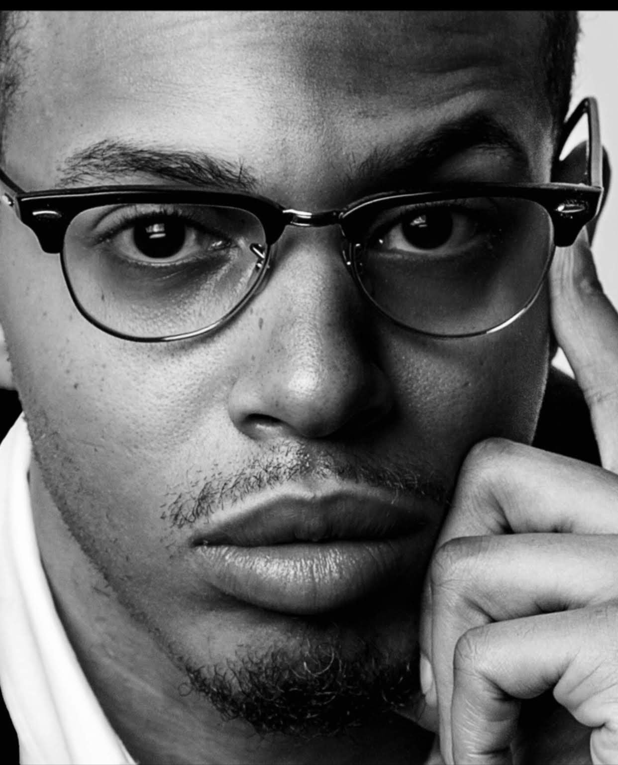 Close-up of a person wearing glasses in black and white, looking directly at the camera.