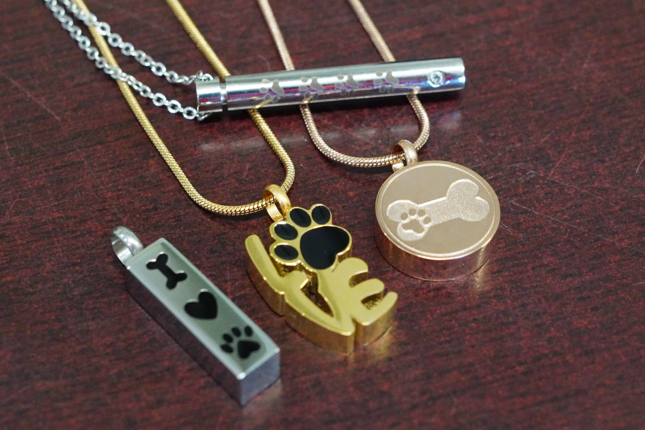 Collection of dog-themed jewelry on a dark wooden surface, including necklaces with dog bone and paw print charms, and a bracelet with bone and paw print designs.