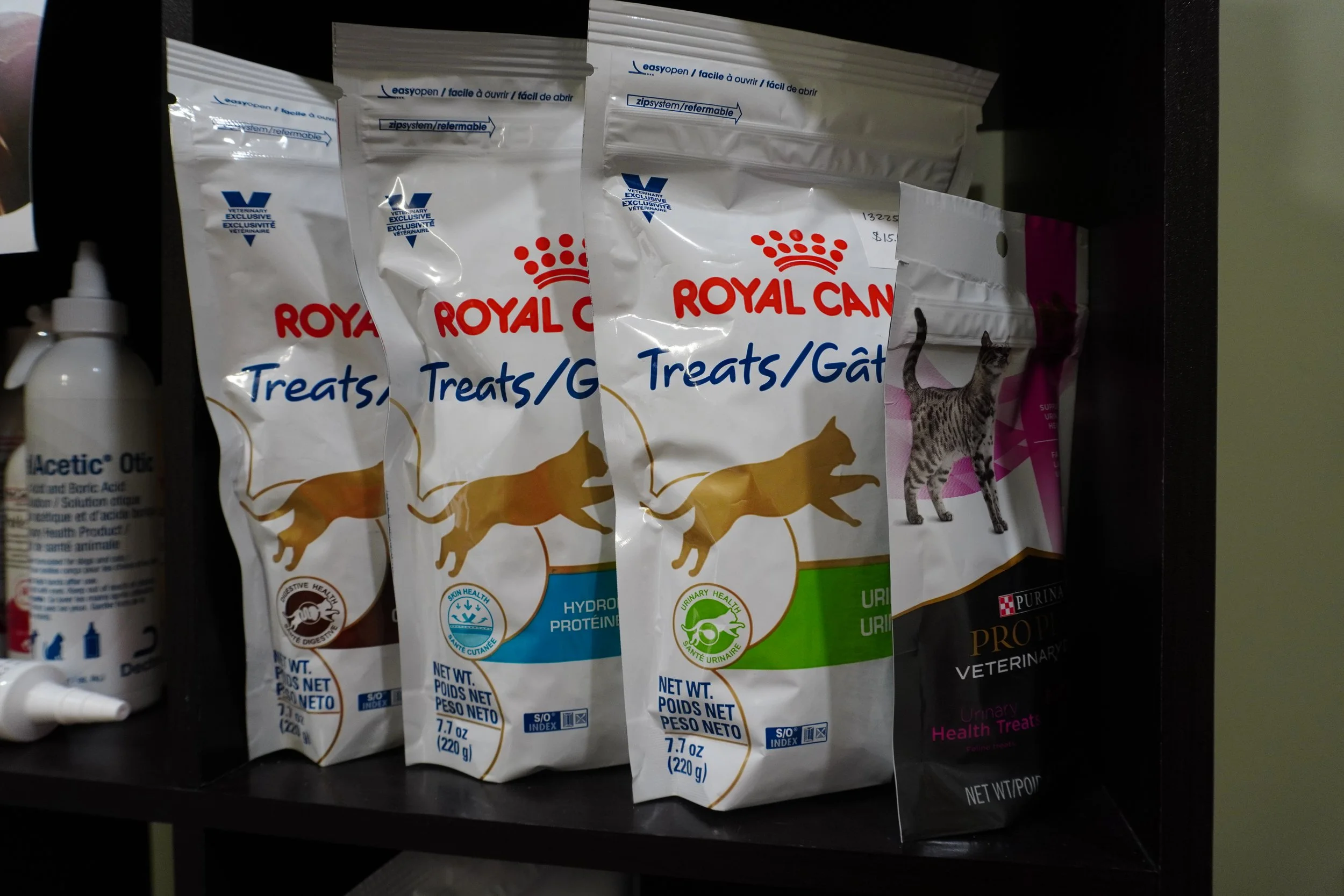 Shelves with bags of Royal Canin pet treats, including different formulas for cats and dogs, and a bottle of medication or supplement on the side.