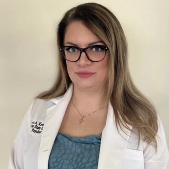 Dr. Lauren Krist DNP, PMHNP-BC; a young woman with blonde hair and glasses, in a white lab coat, against a light background.